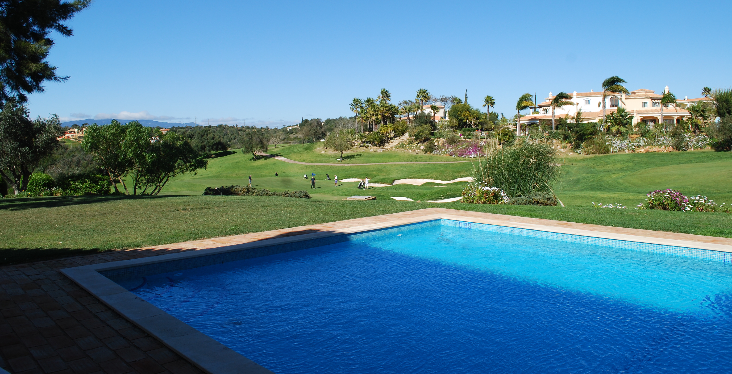 Outdoor pool of Pestana Gramacho Residences, overlooking the golf course, with several trees and palm trees