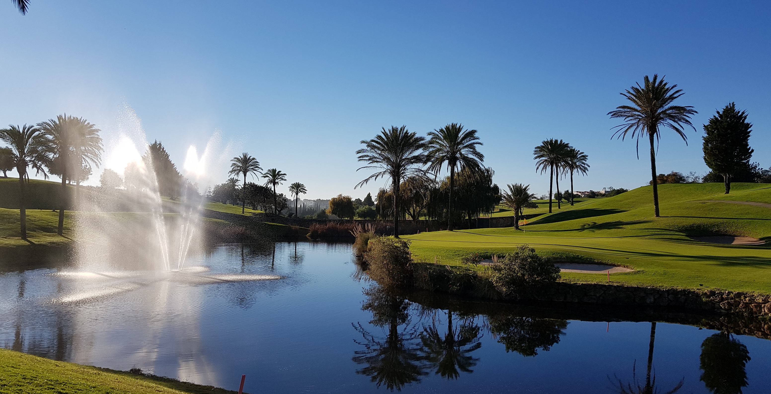 Lake with central fountain on Pestana Gramacho Residences golf course, with scattered palms and reflections