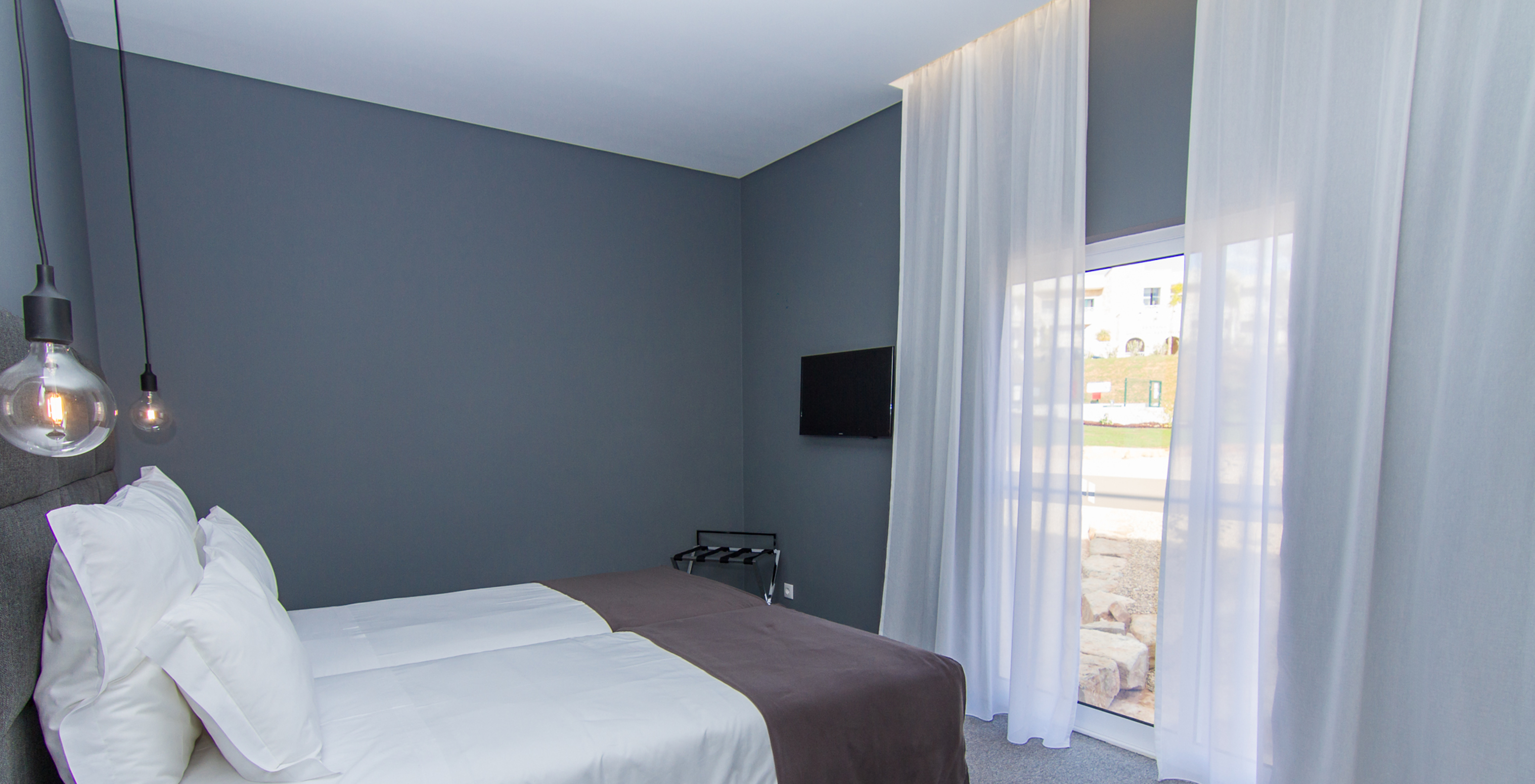 The Classic room at Pestana Gramacho Residences features two single beds, a television, and a window with curtains