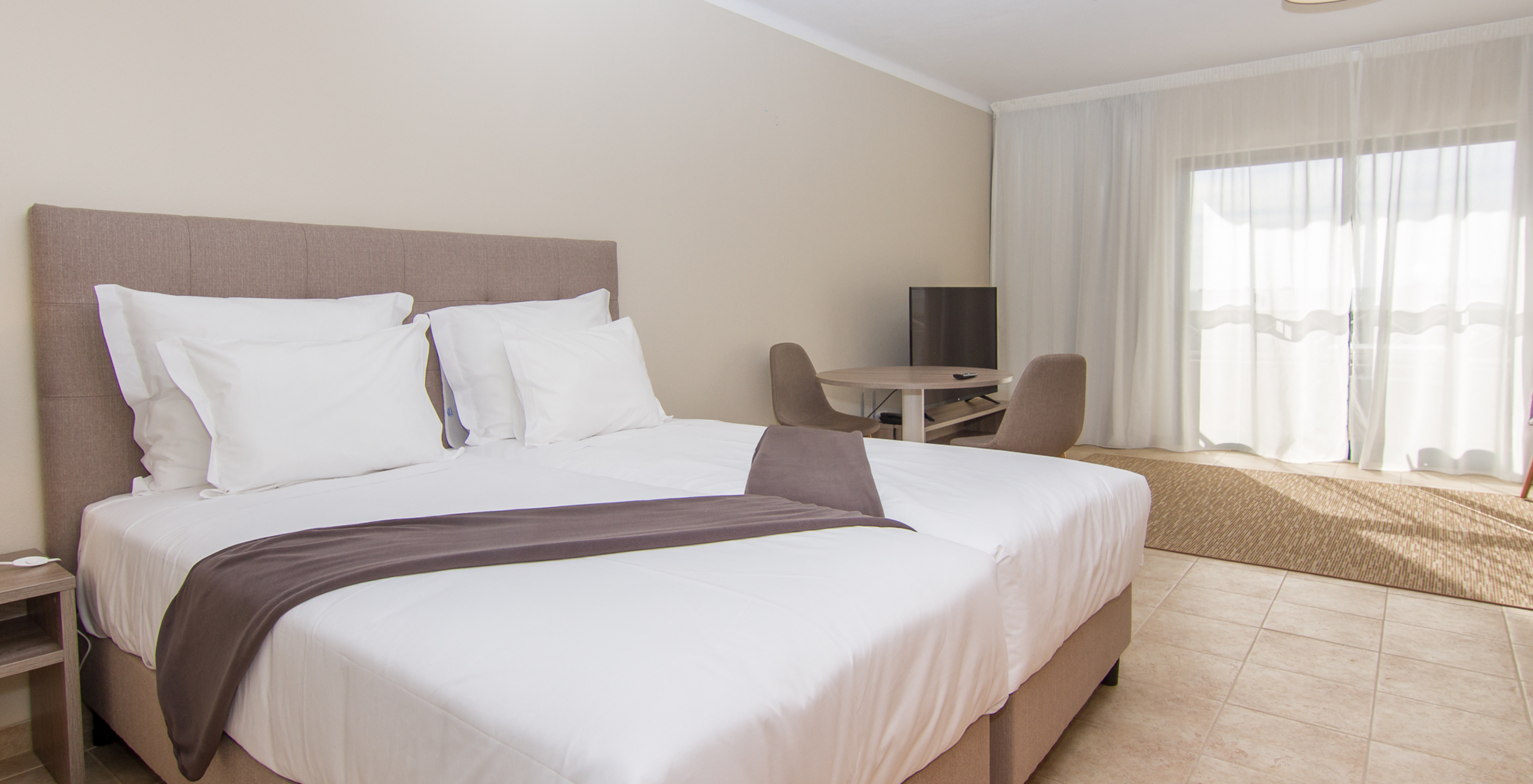 The Studio at Pestana Gramacho Residences features two single beds, a table with two chairs, and a window