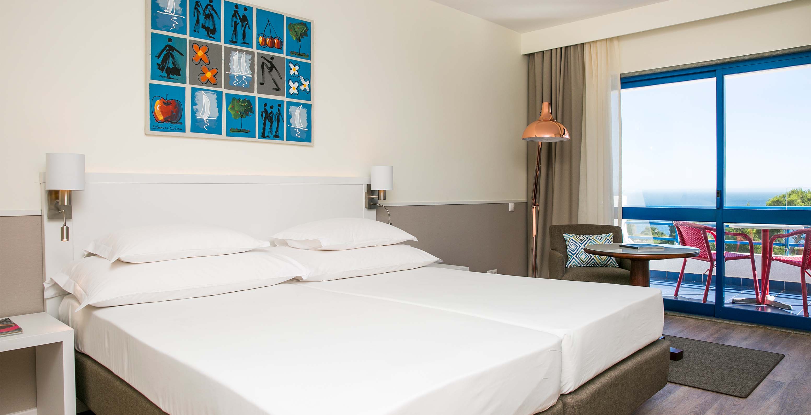 The Deluxe Sea View room at Pestana Cascais has two single beds, bedside lamps, and an armchair with a table