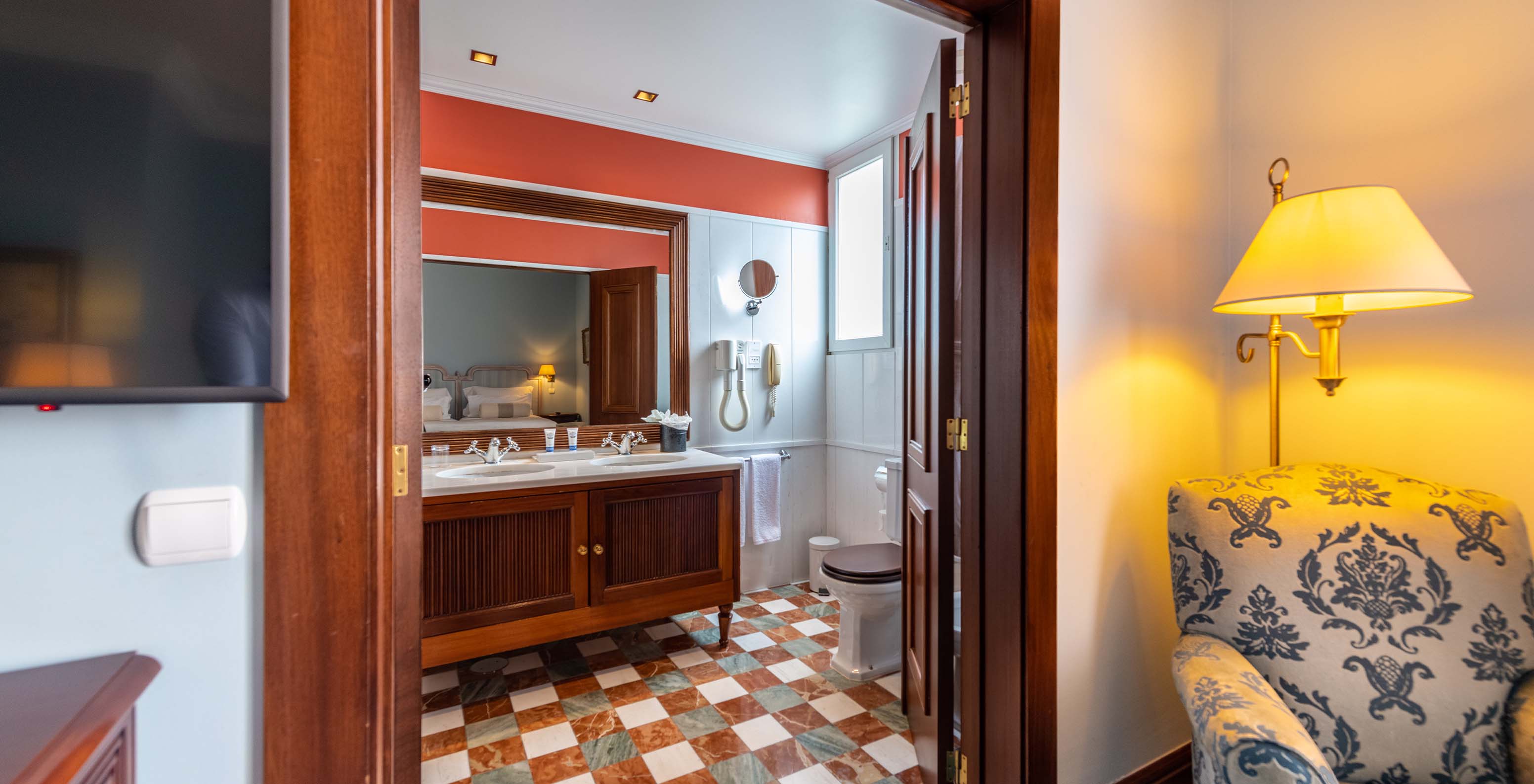 The Deluxe room at Pestana Palace Lisbon features a bathroom with two sinks in a wooden cabinet, a mirror, and a toilet