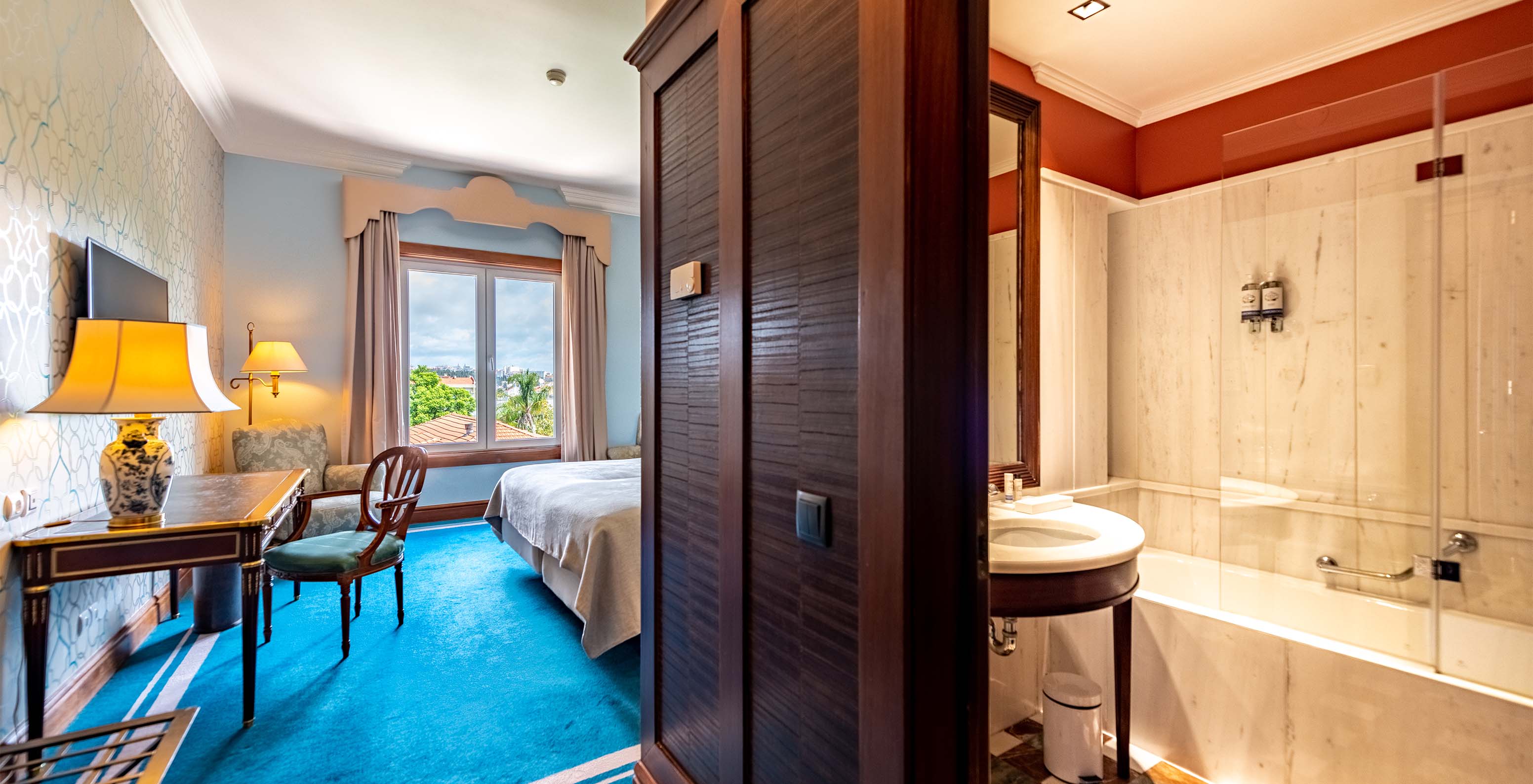 The Deluxe Garden room at Pestana Palace Lisbon includes an entrance hallway, a wooden desk, television, and a window