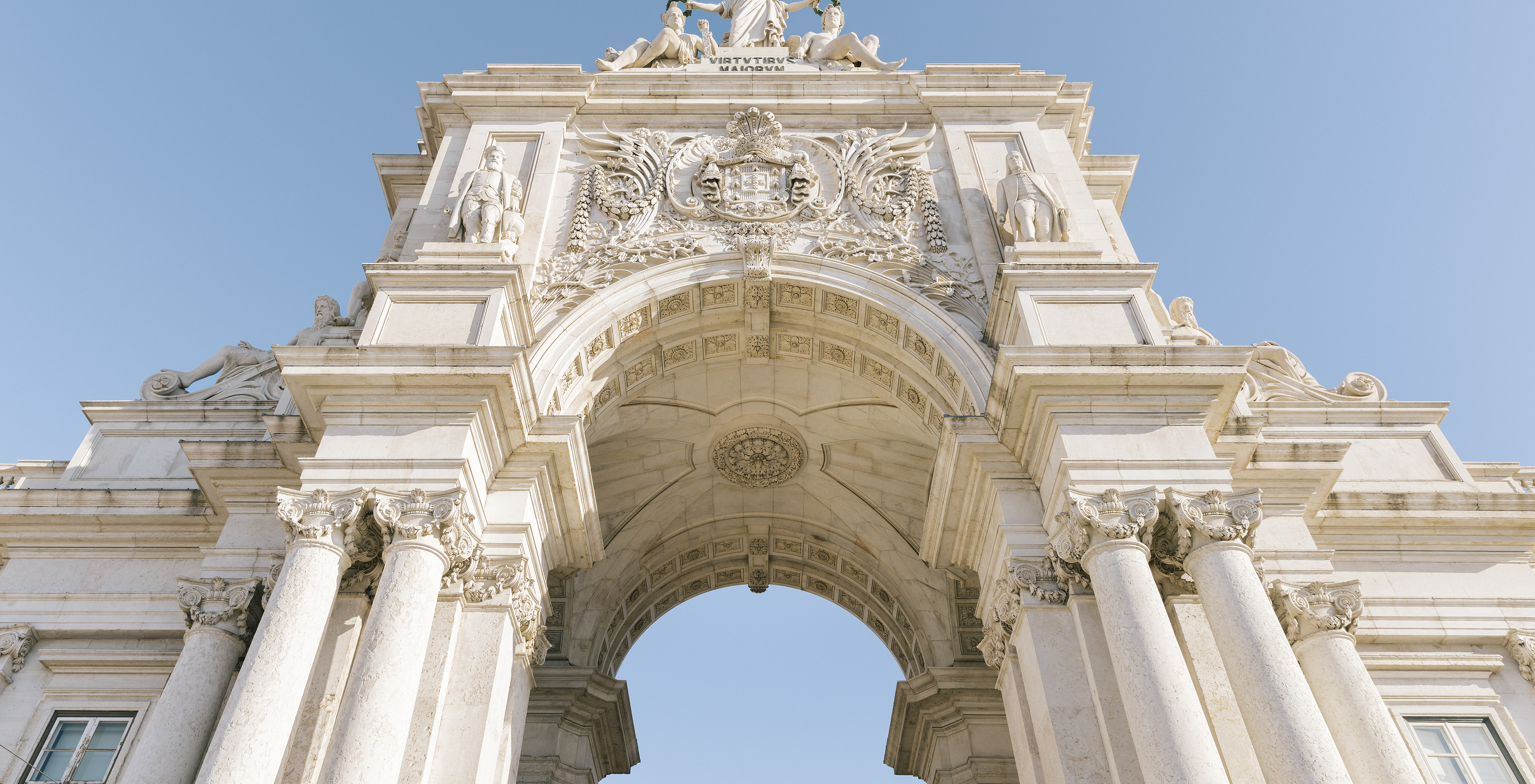 Arco da Rua Augusta in Lisbon with neoclassical architecture, details like columns, statues, and Portugal's coat of arms