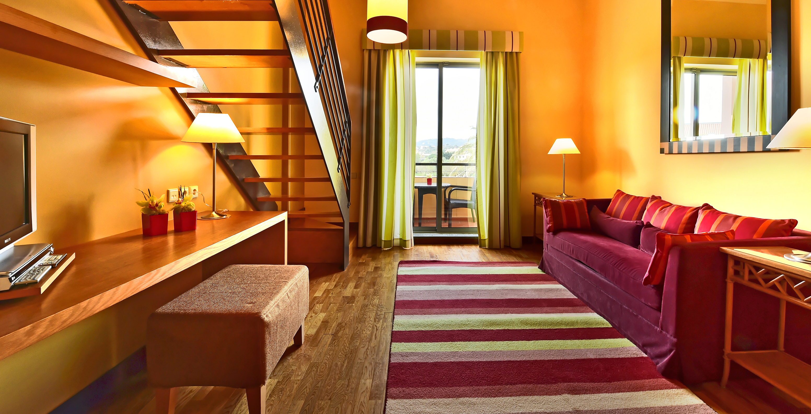 The Family Mezzanine Suite of Pestana Sintra Golf has a room with a large sofa, mirror, and a window with balcony access