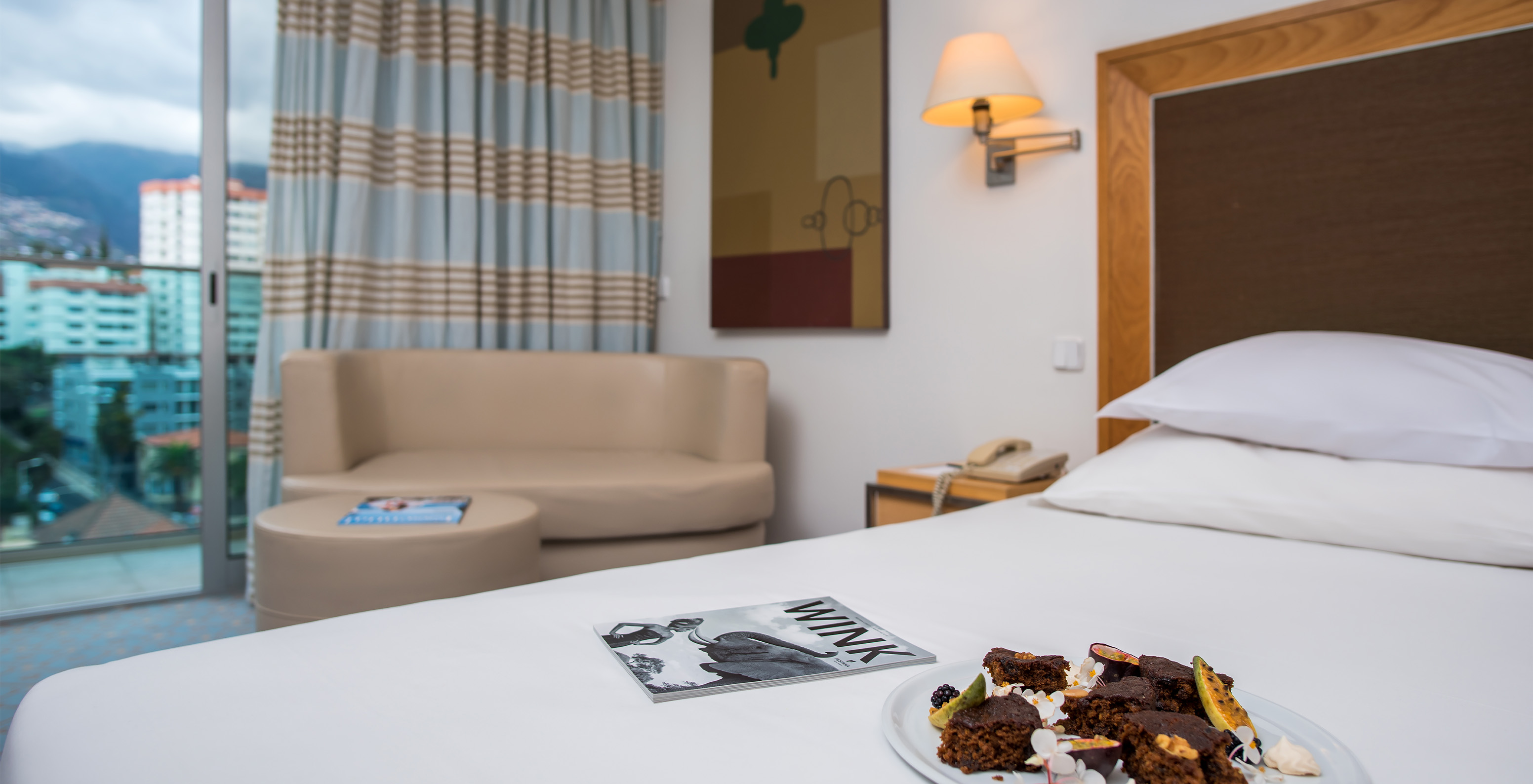 The Suite at Pestana Carlton Madeira has a bed with a plate of chocolate and fruit on it