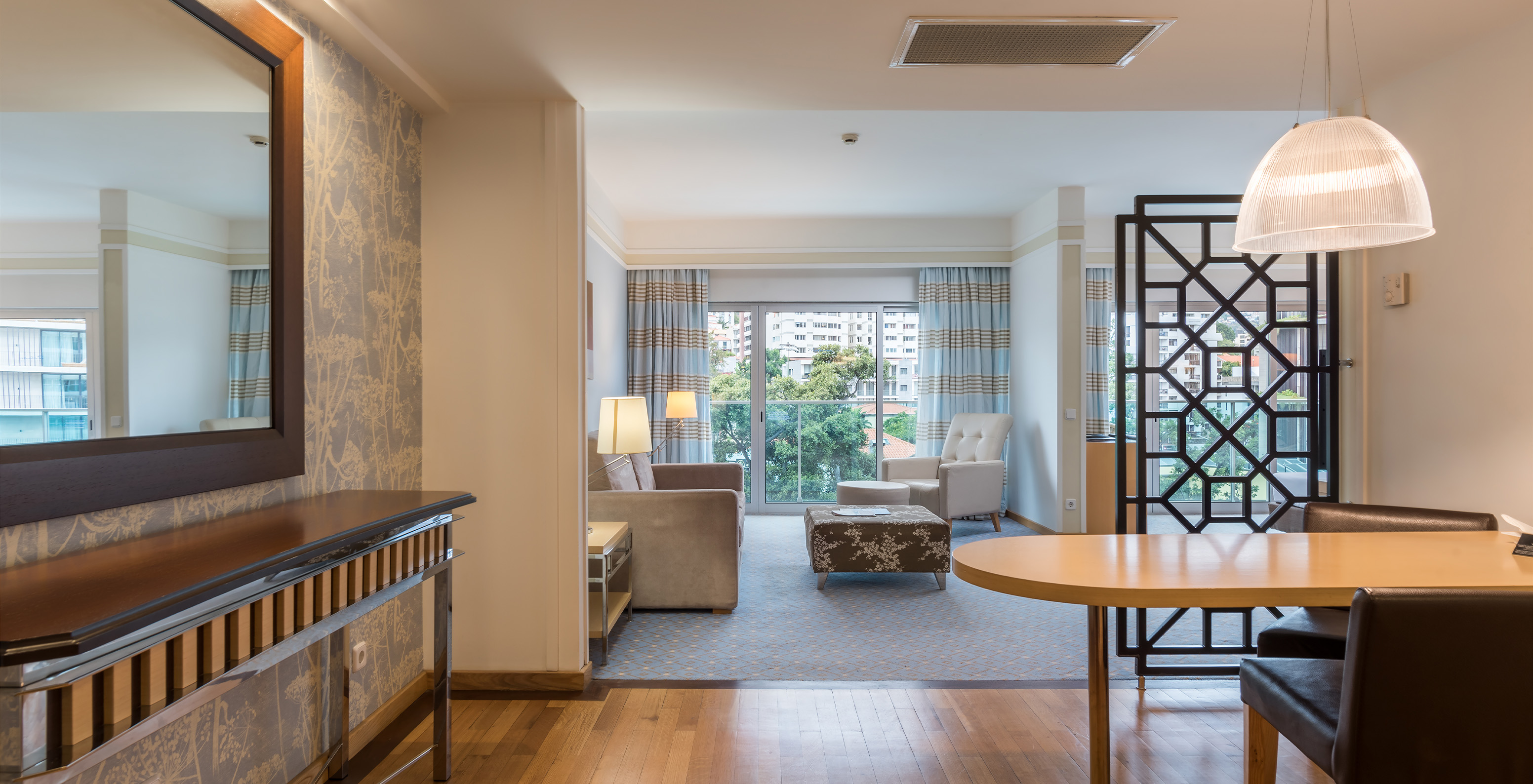 The Family Double Room at Pestana Carlton Madeira has a large entrance with a table and chairs, a mirror, and sofas