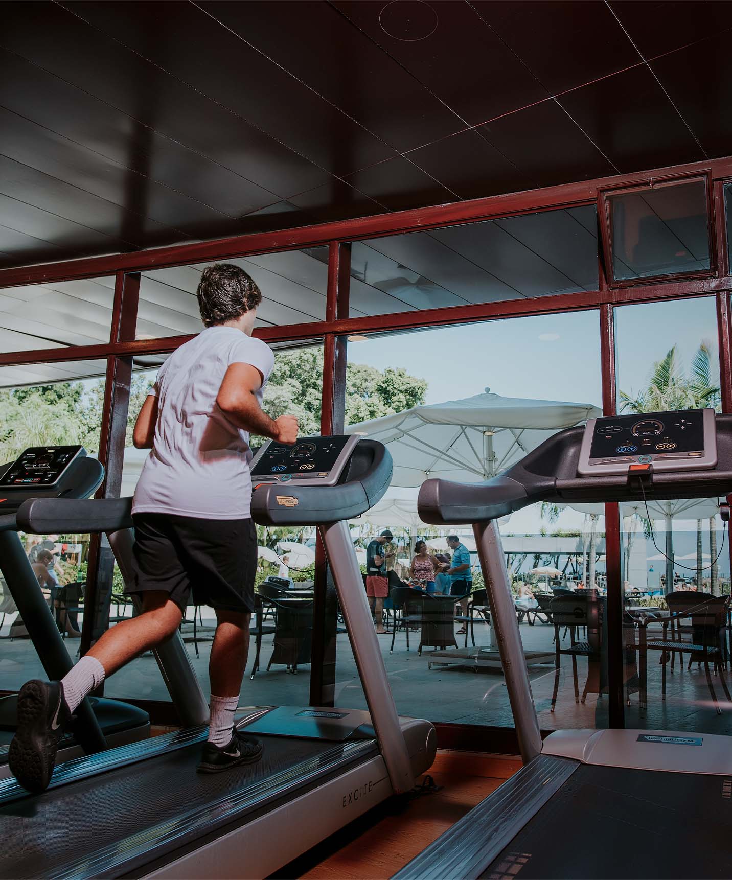 Boy running on the gym treadmill overlooking the terrace of the hotel in Funchal with spa and pool