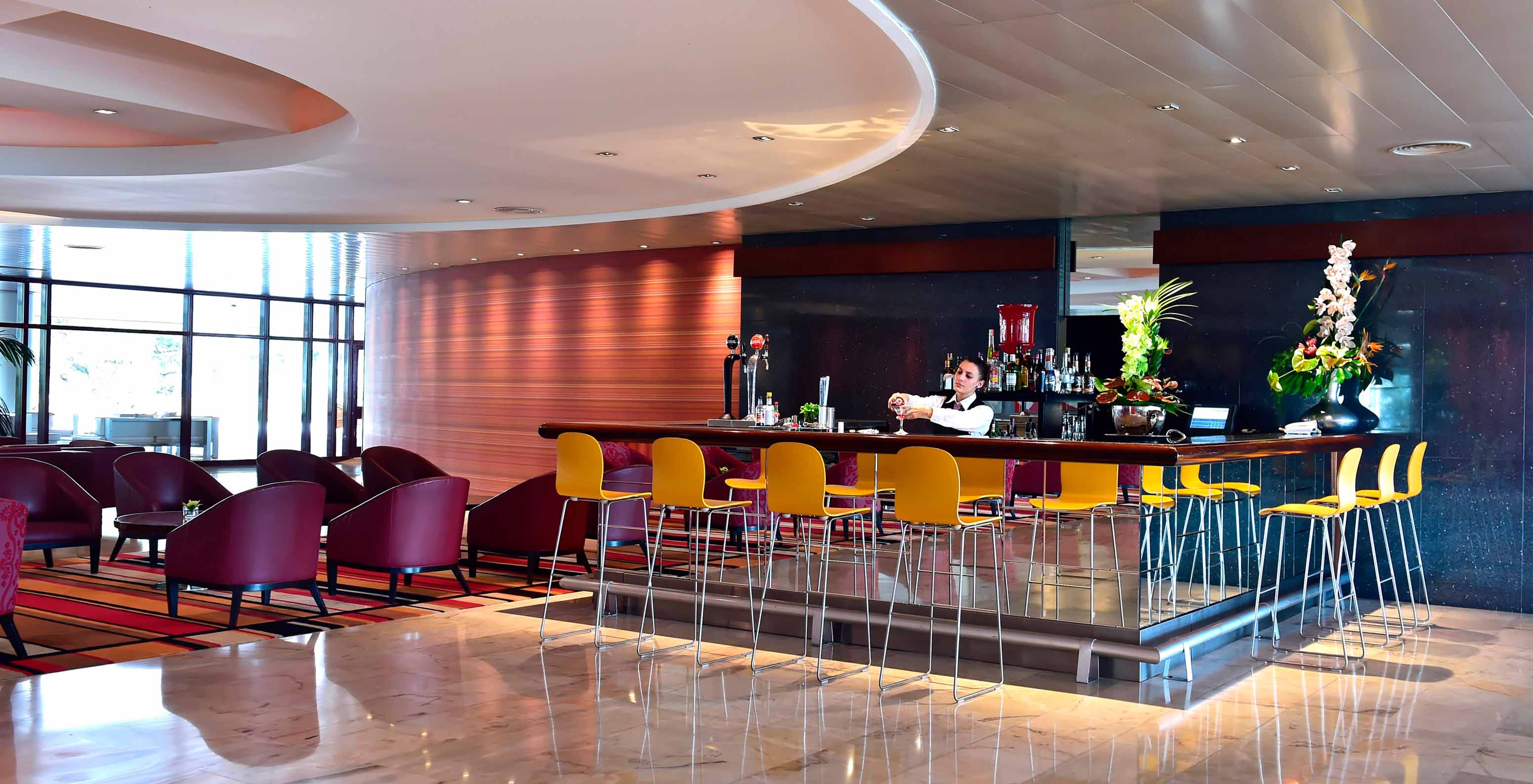 Hotel bar area in Funchal by the sea, with a spa and pool, and a lady serving drinks at the counter