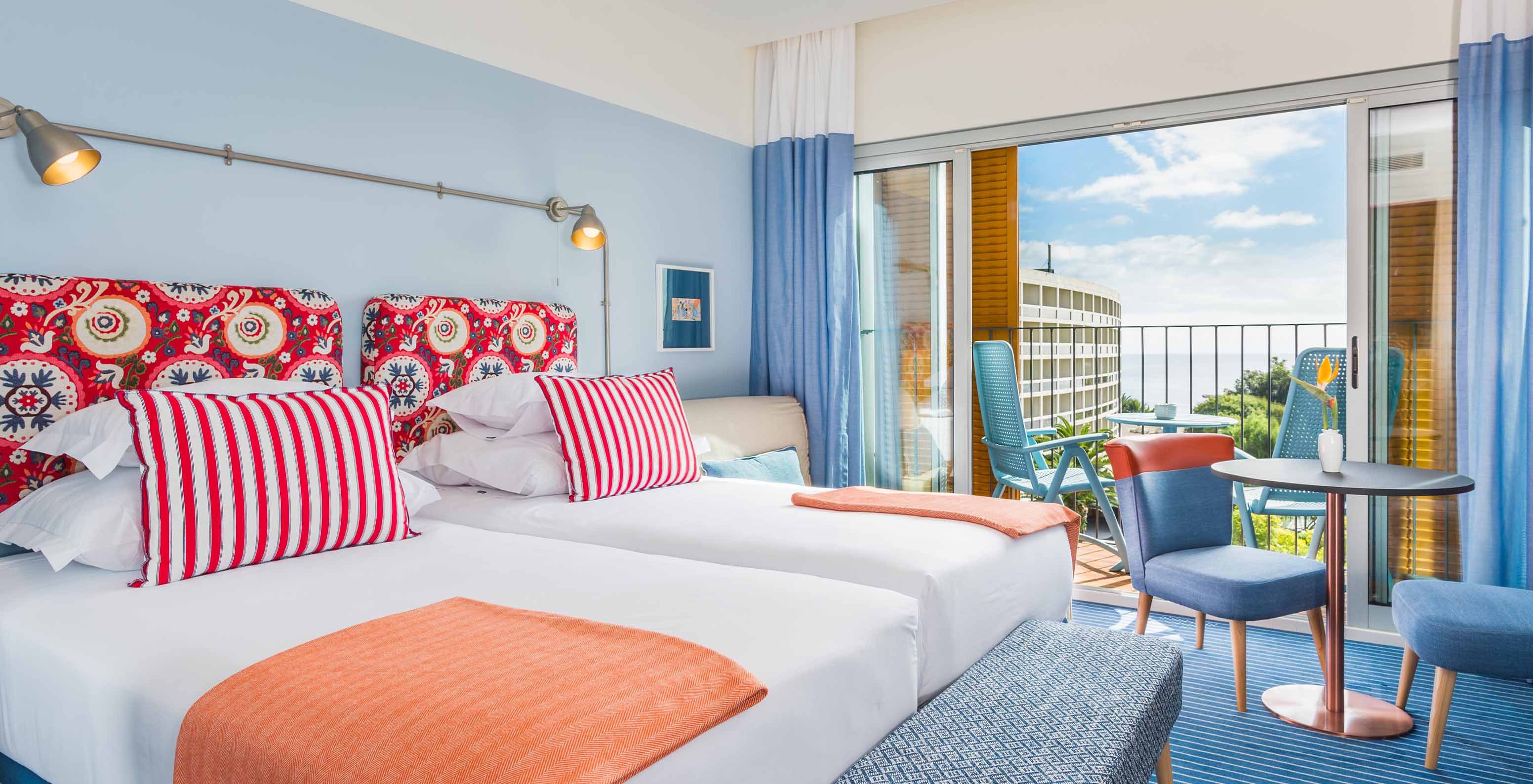 The Sea View Deluxe Studio at Pestana Casino Studios has two double beds with a patterned headboard, a balcony, and a table