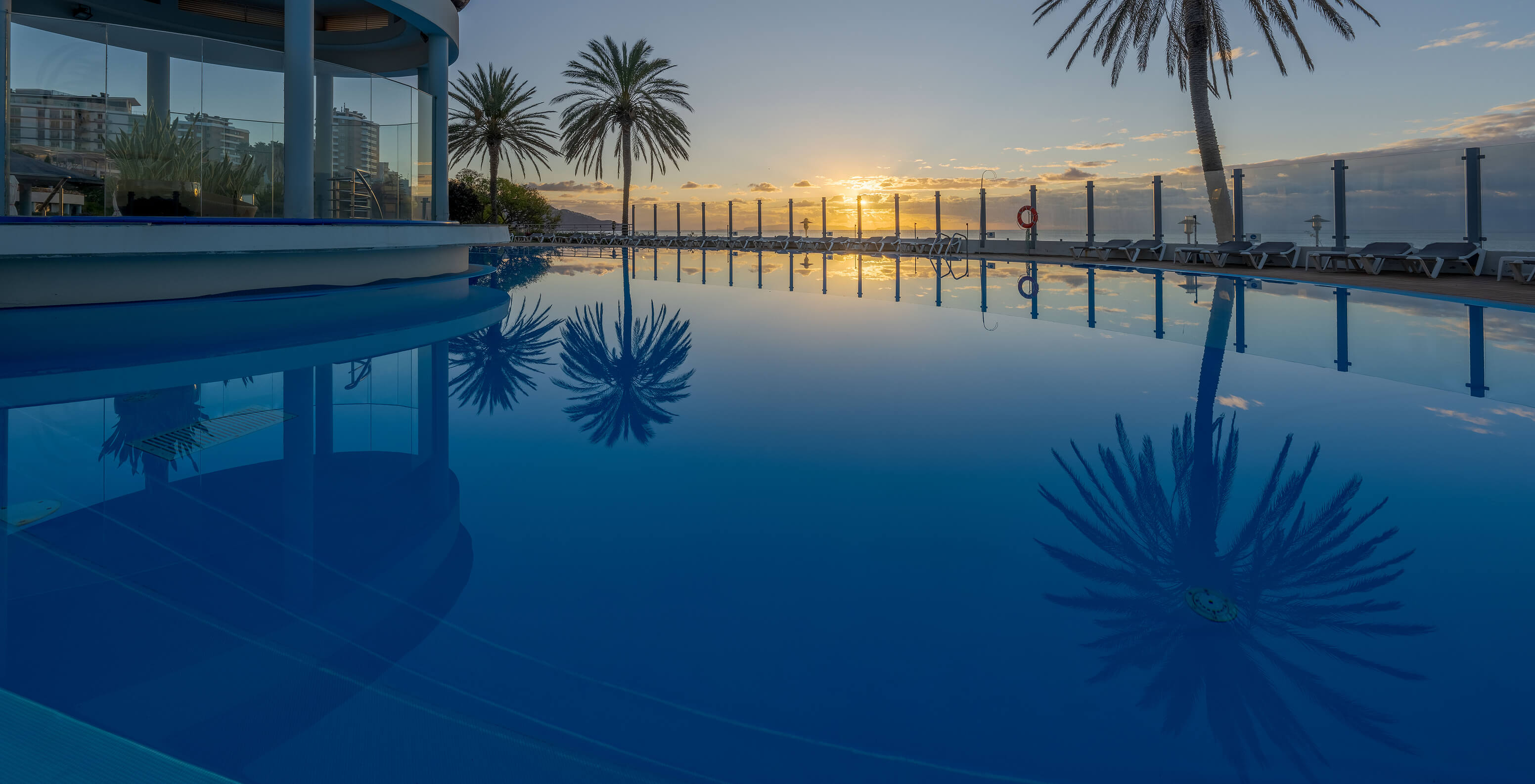 Outdoor pool at Pestana Grand, surrounded by palm trees and overlooking the ocean, where you can see the sunset