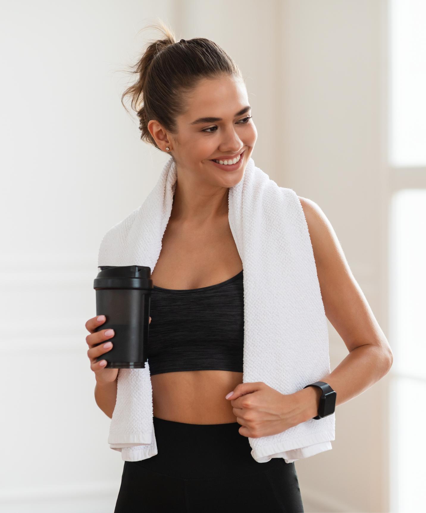 Woman at the Premium Resort with Spa and Pool, facing the sea, exercising with a towel around her neck and a smoothie