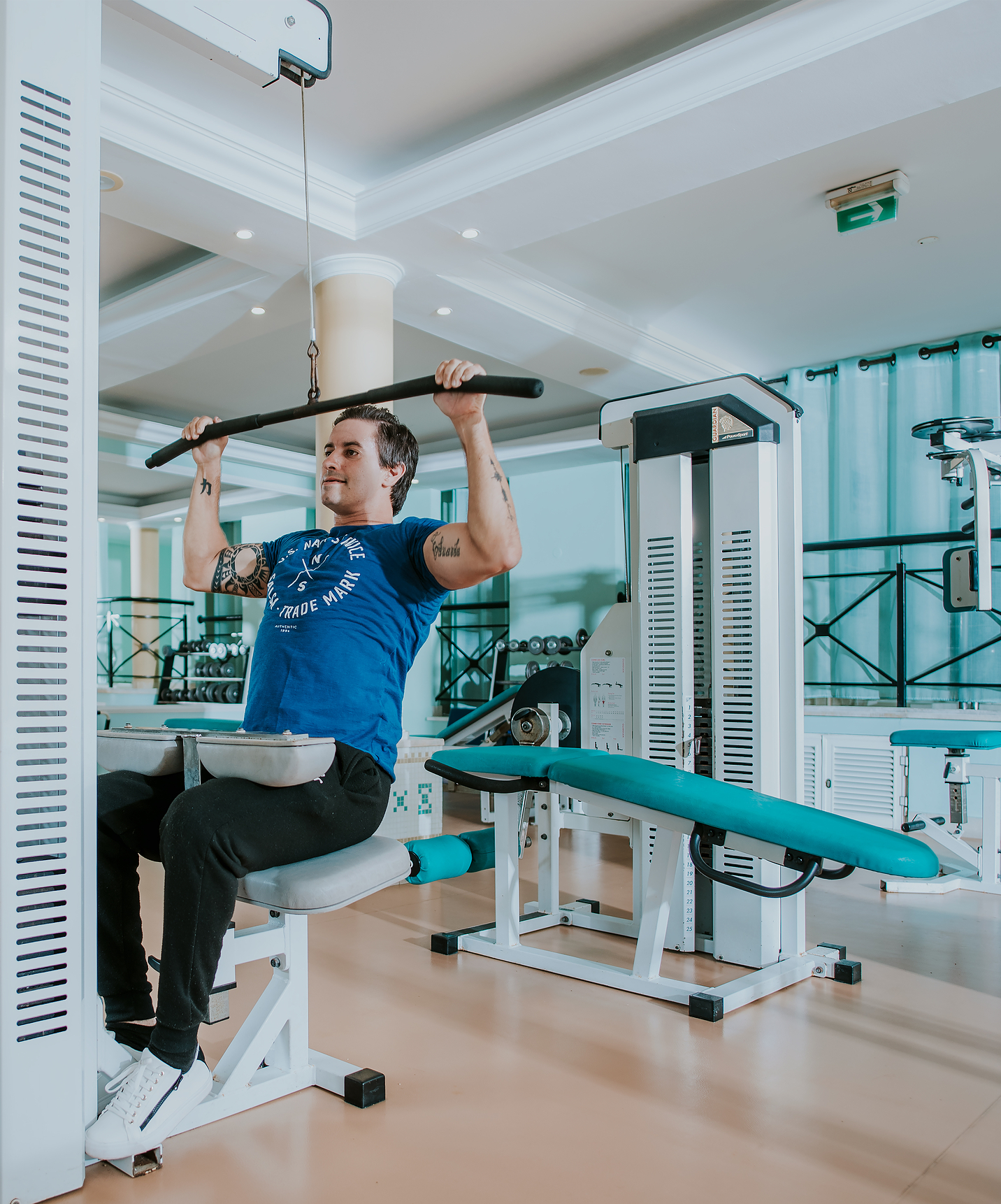 Man using an arm strength machine at the gym of Pestana Miramar, a hotel in Madeira near the beach, with a pool