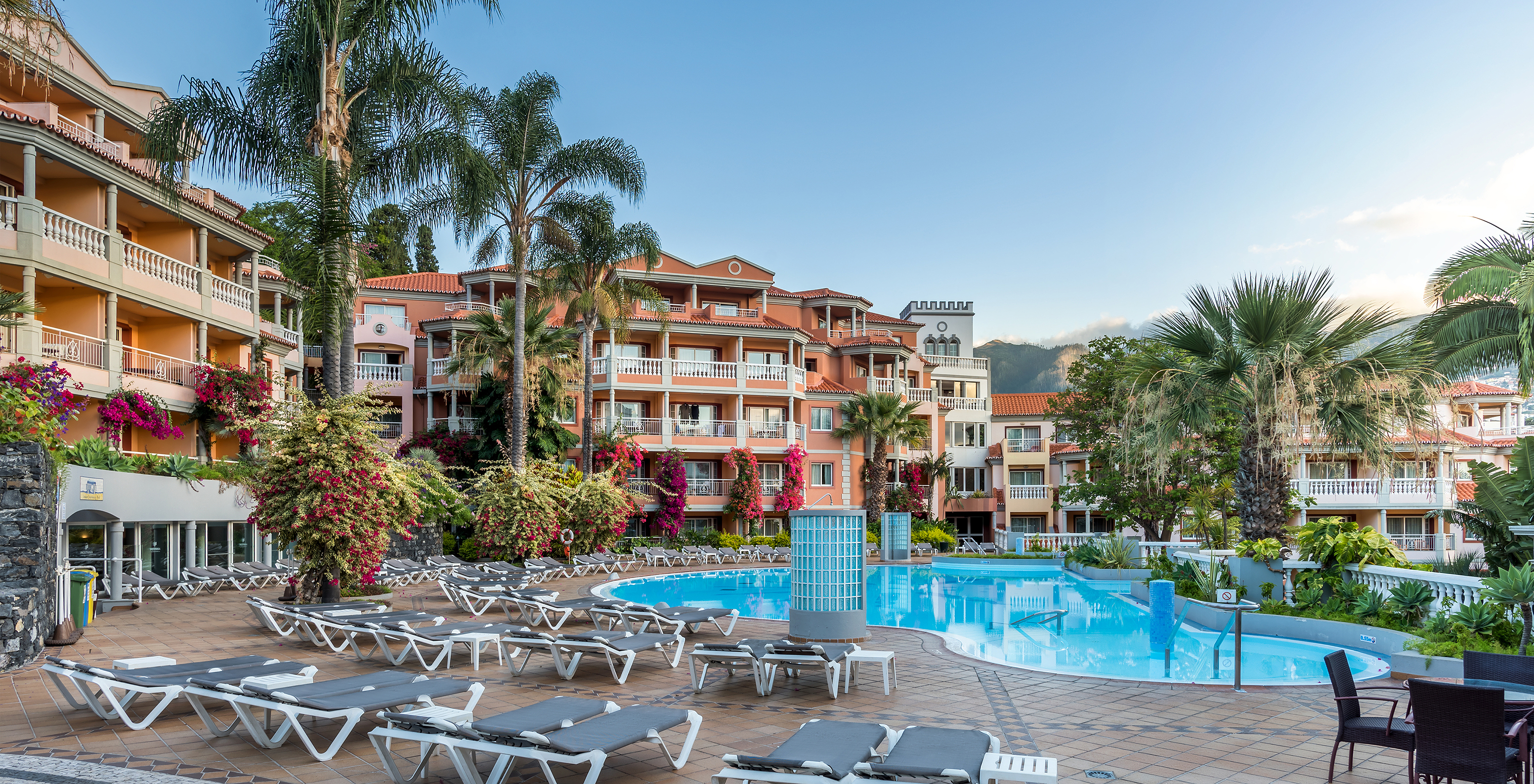 Exterior of Pestana Miramar, a hotel in Madeira near the beach, with pool surrounded by palm trees and several buildings