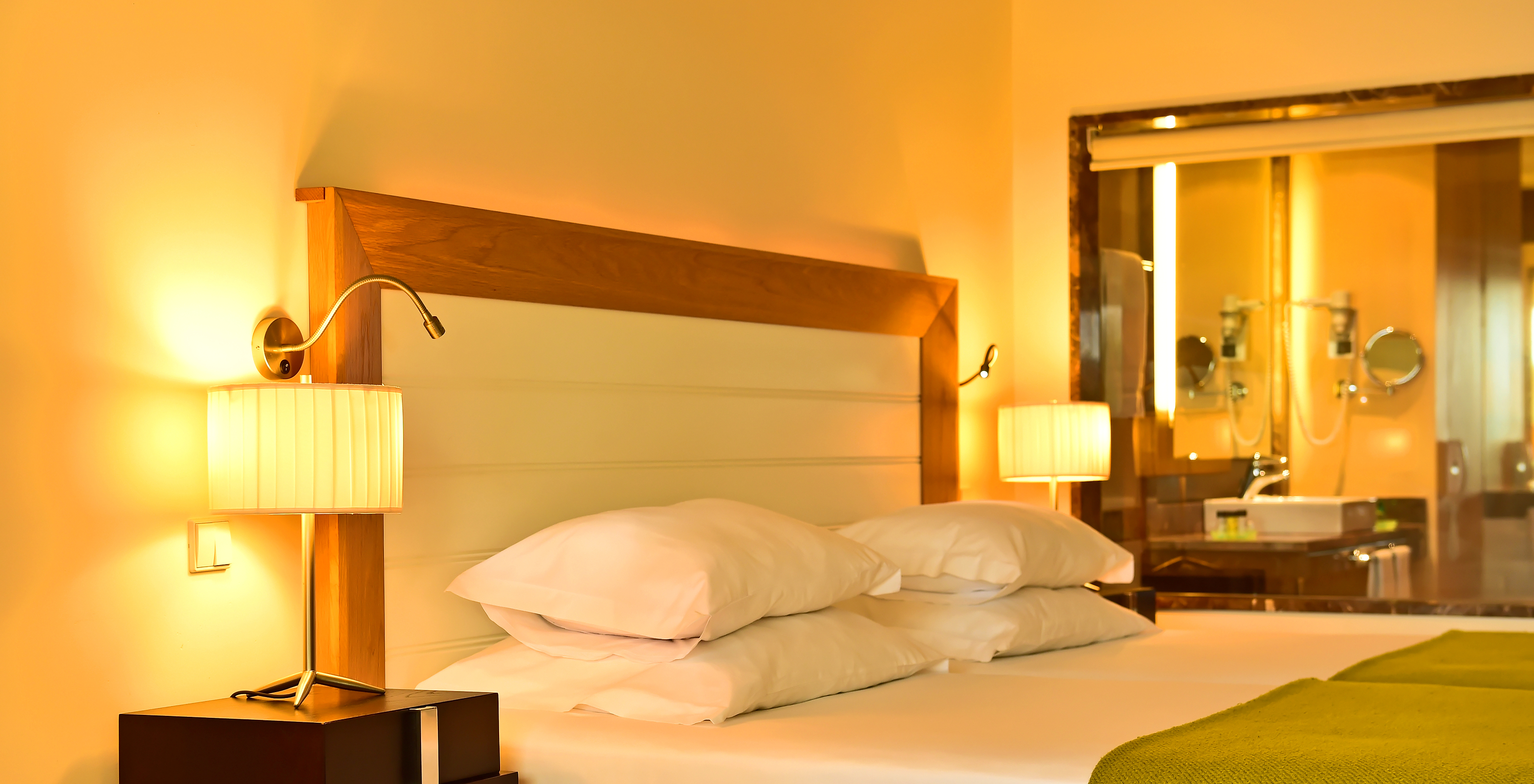 The Classic of Pestana Promenade has a bed with a green bedspread, lamps on the nightstand, and a bathroom at the back