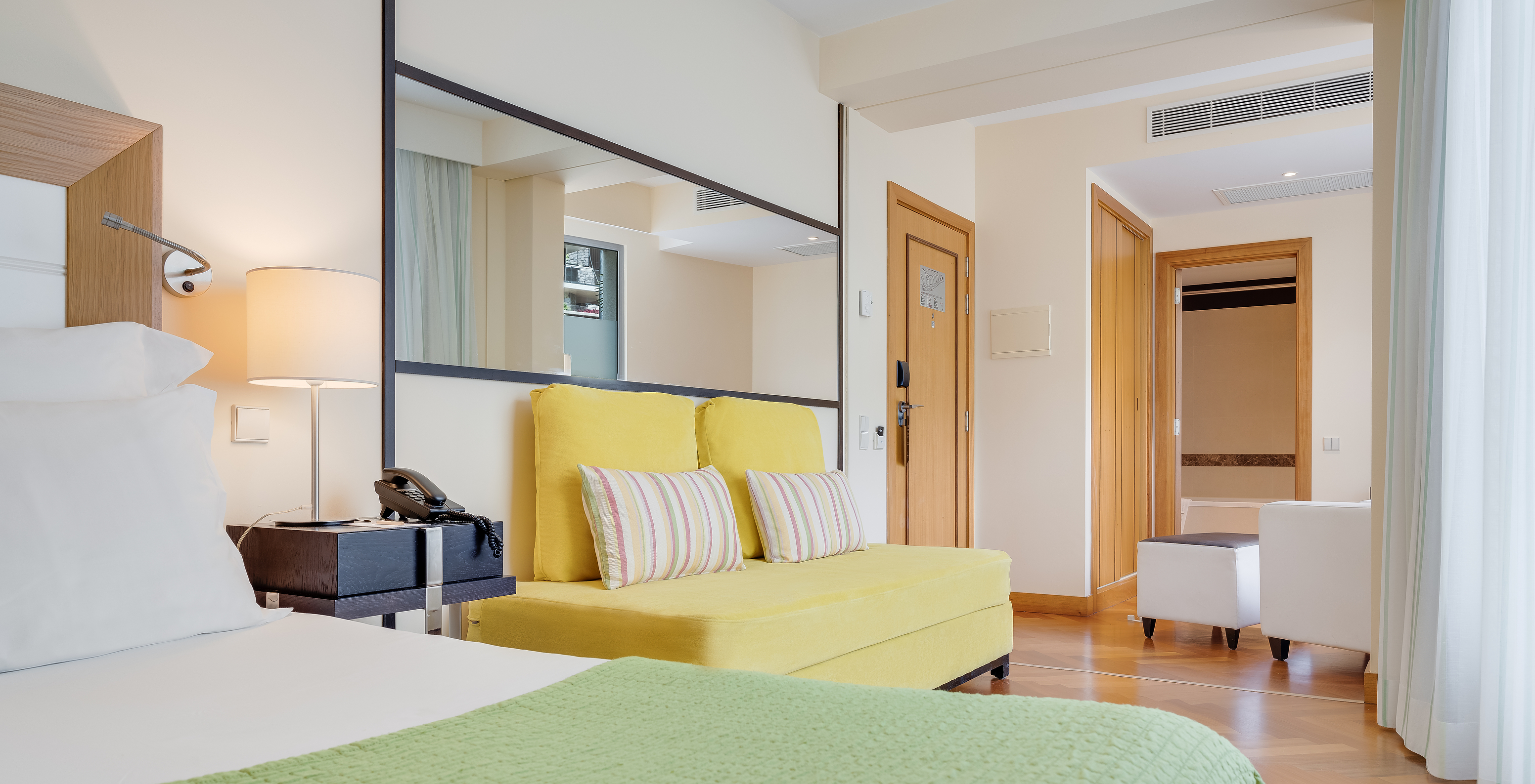 The Classic Twin of Pestana Promenade has a double bed, a yellow sofa, and a large mirror on the wall