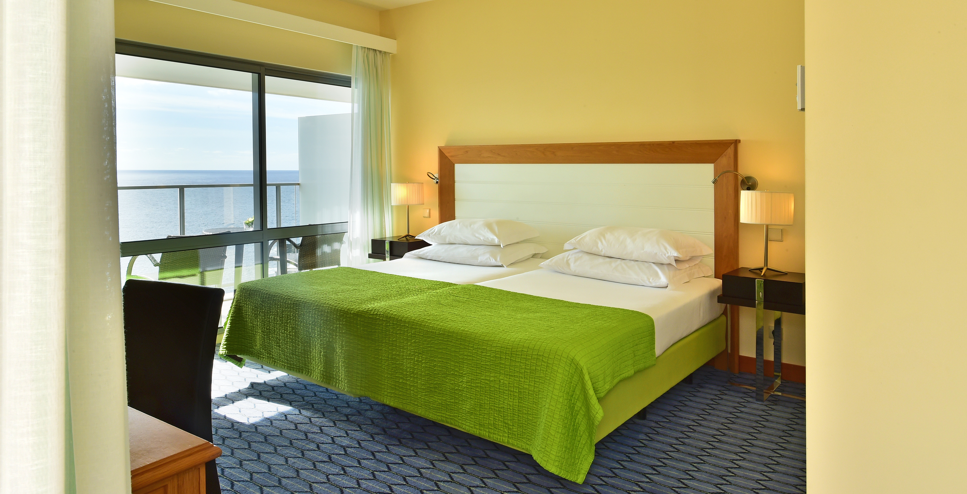 The Suite Sea View of Pestana Promenade has a double bed with a green bedspread and a large window to the balcony