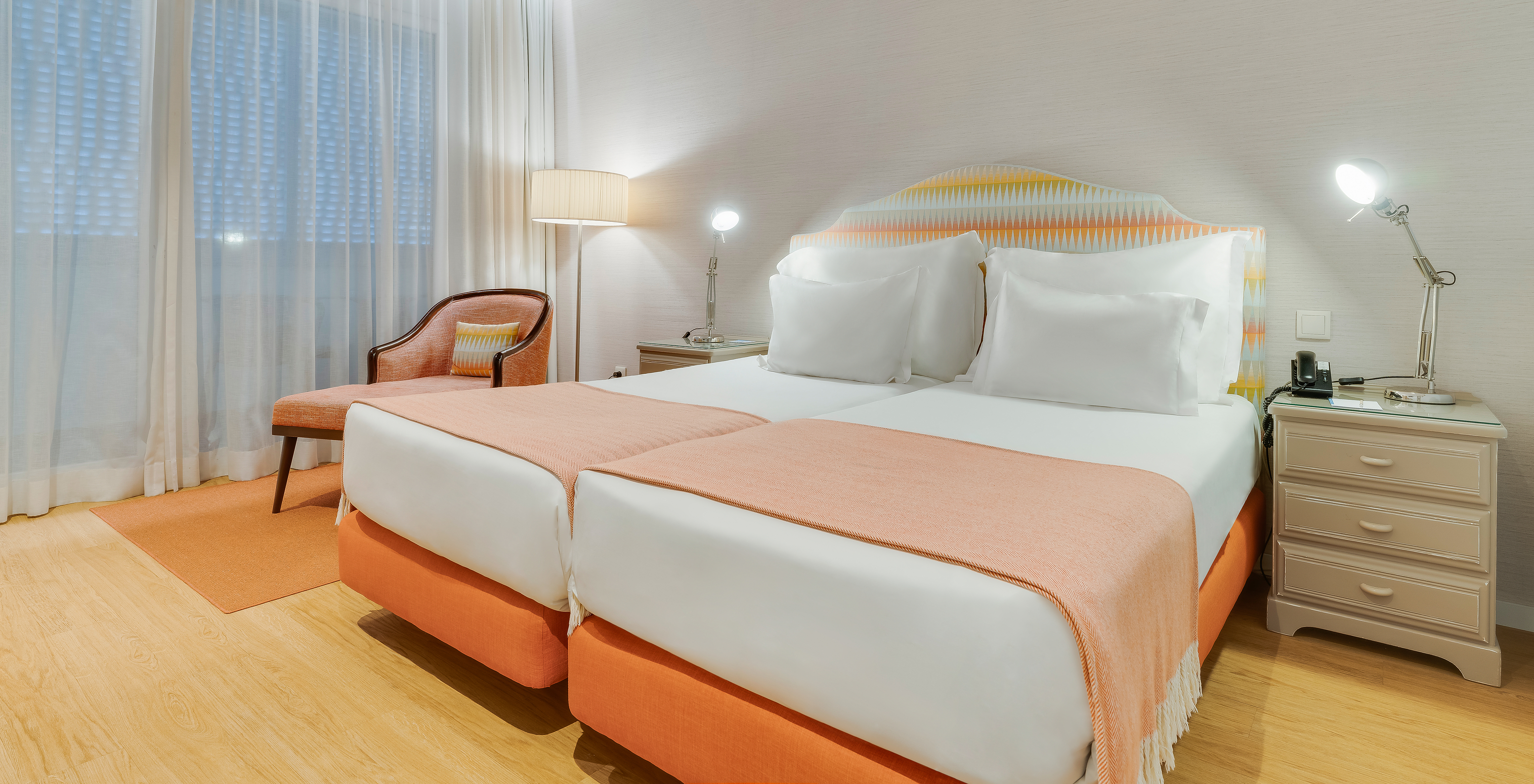 The Classic Twin Promenade View of Pestana Promenade has two beds in orange tones, an armchair, and nightstands