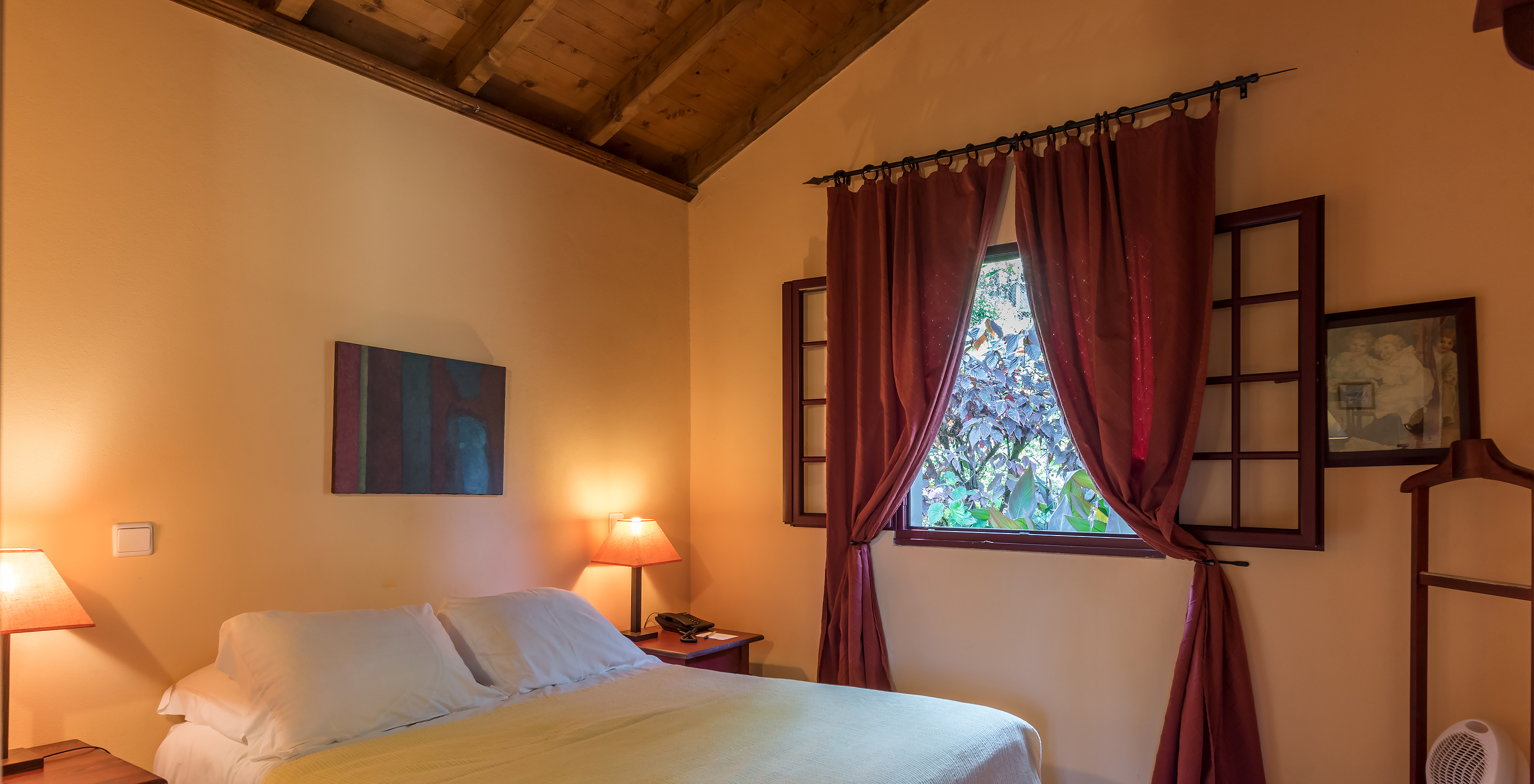 The Villas of Pestana Quinta do Arco have a double bed with a window to the garden with red curtains and stone floor