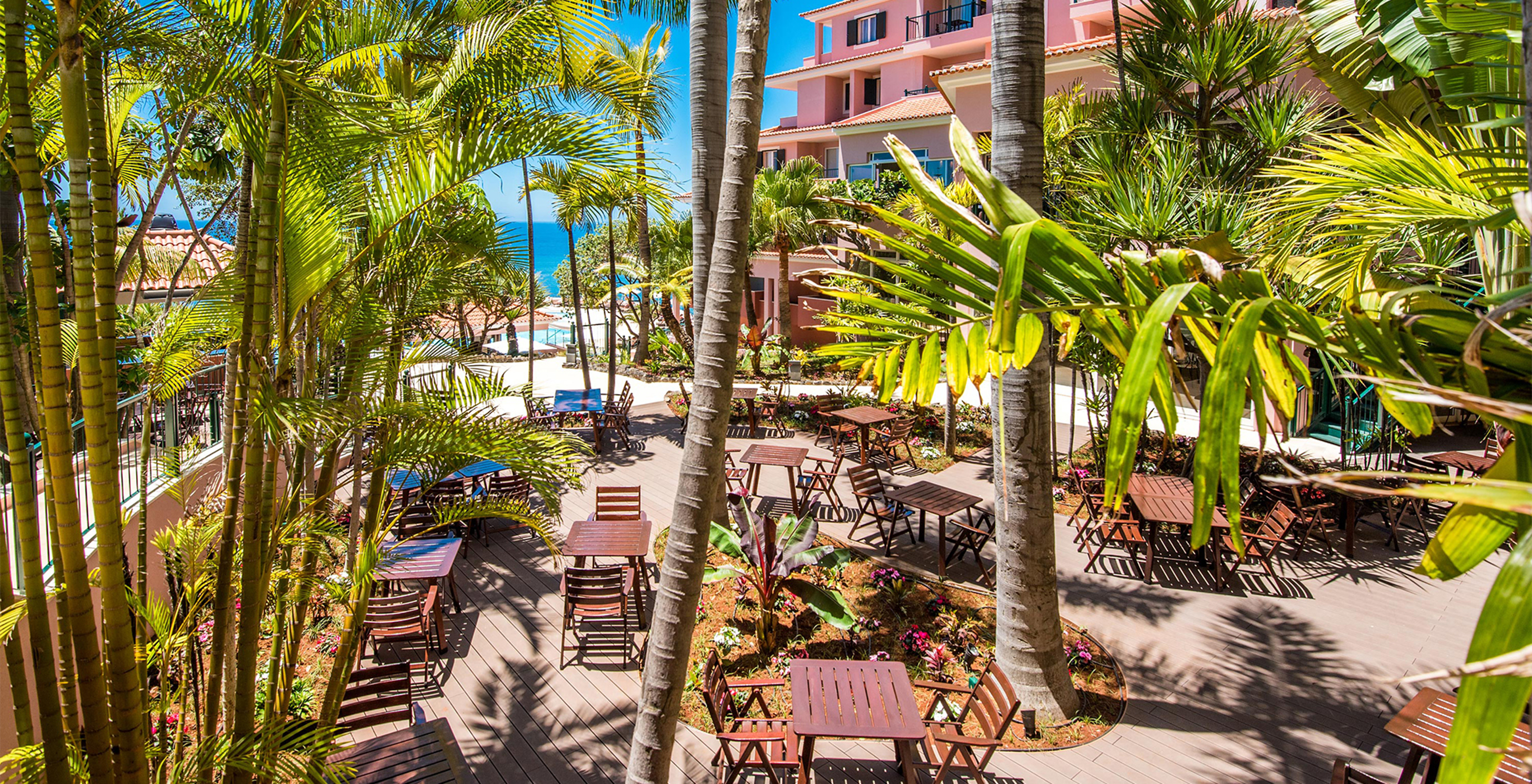 Pestana Royal All Inclusive, hotel near the beach, has a garden with palm trees, chairs, and tables