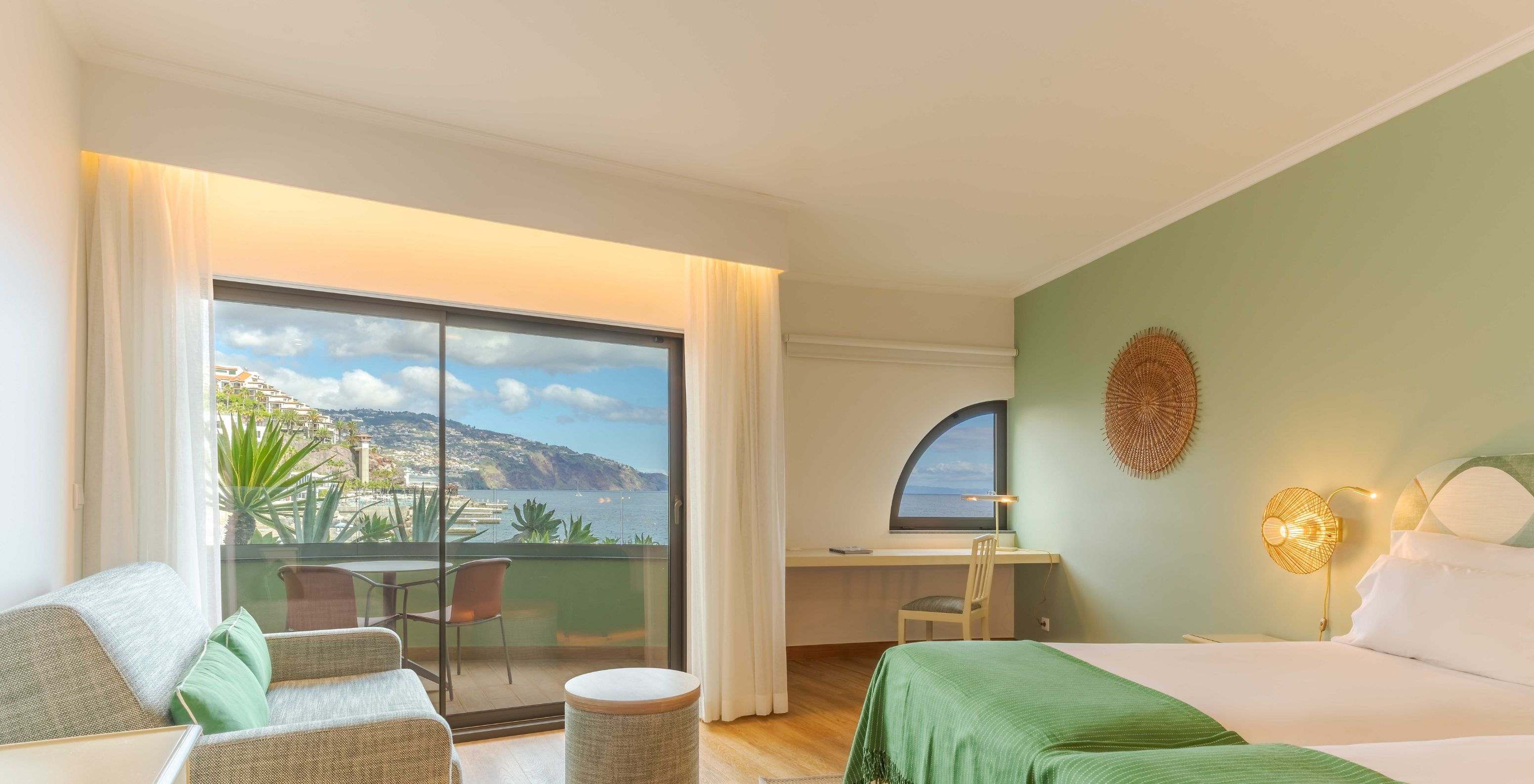 The Superior Lateral Sea View room at Pestana Vila Lido Madeira features a large window overlooking the balcony, a desk and a sofa