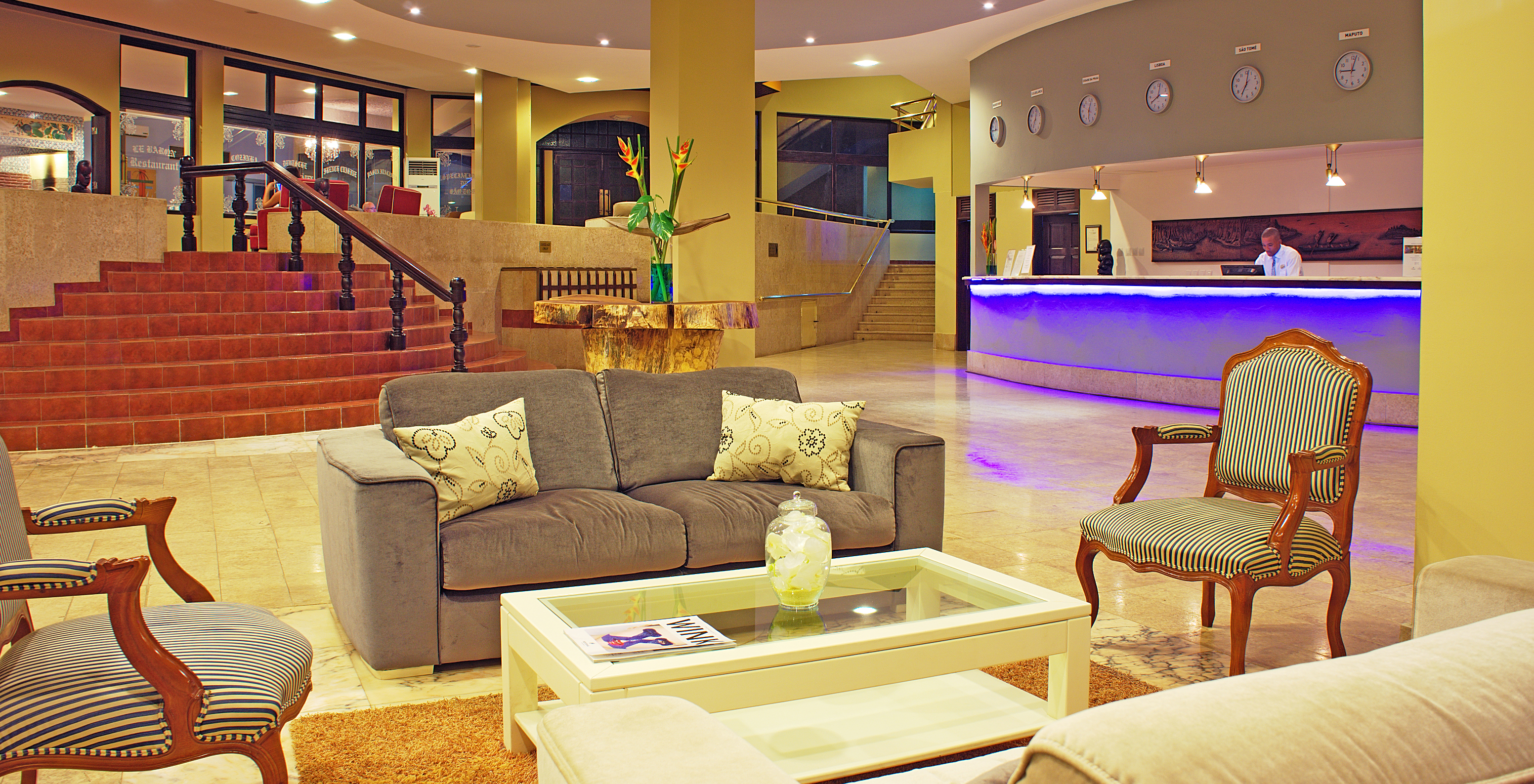 Spacious lobby with sofas, chairs and staff member working at the reception of hotel with pool, beachfront