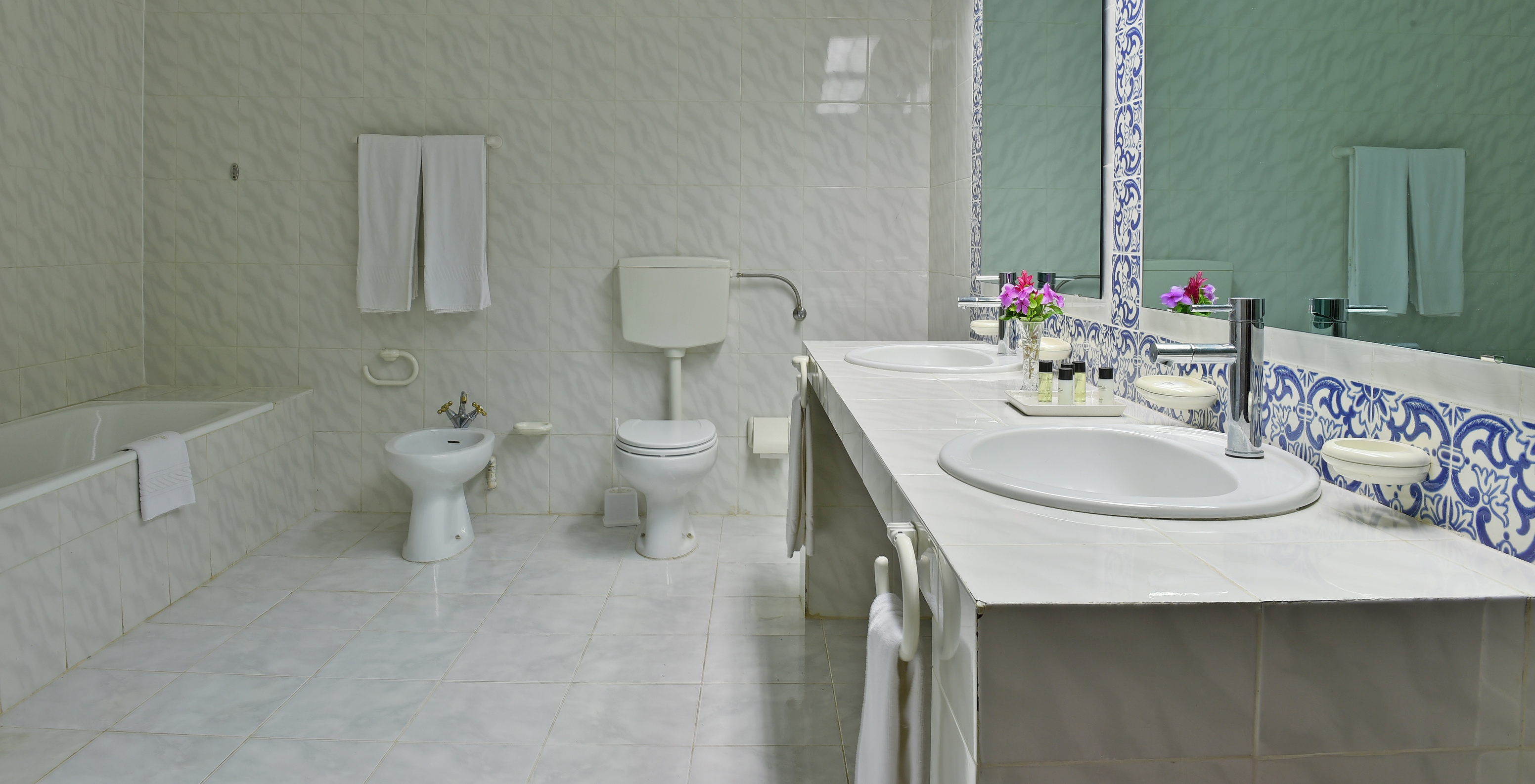 The Junior Suite at Pestana Miramar São Tomé features a bathroom with tiled walls, sinks, mirrors, a bidet, and a toilet