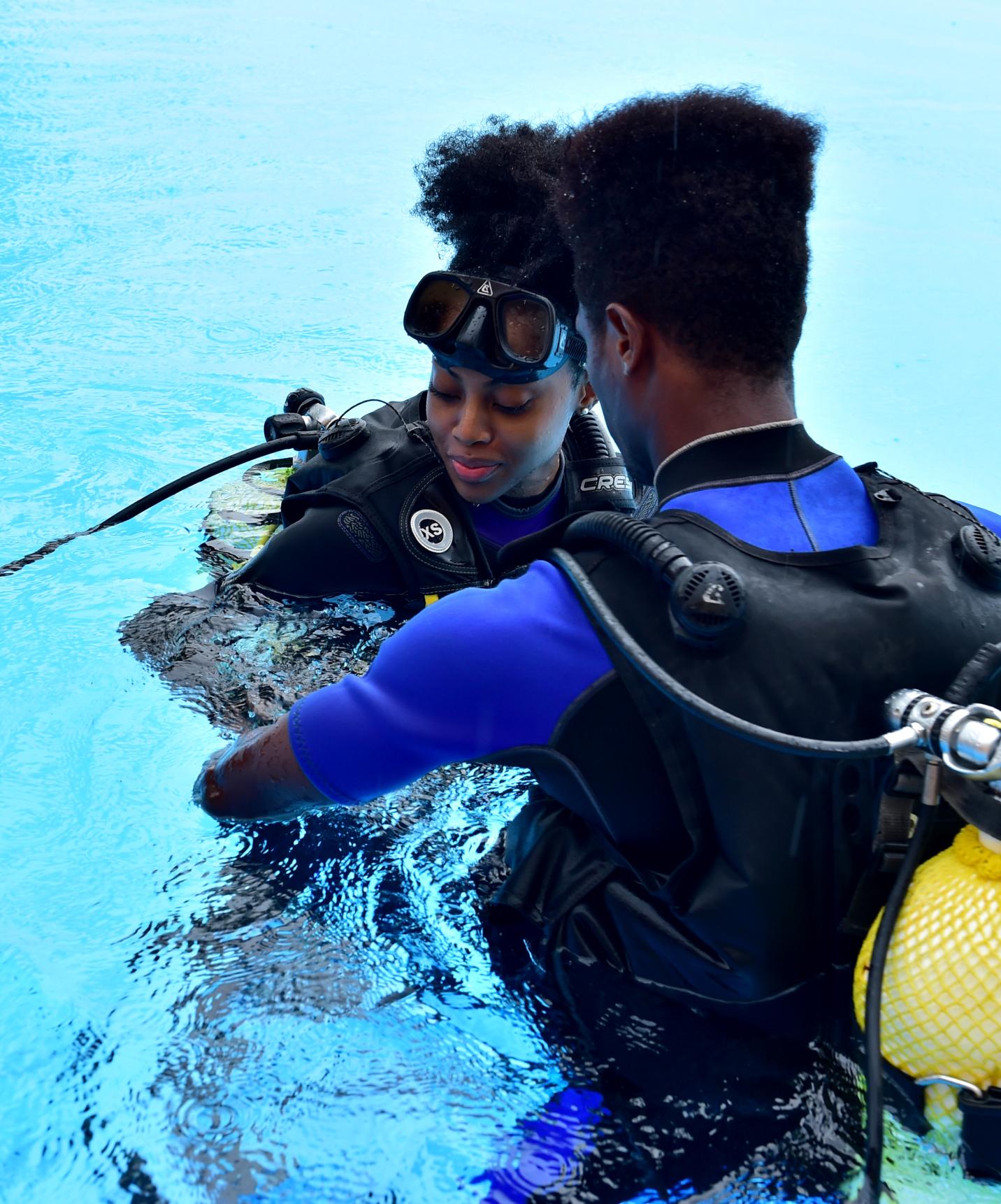 Two people getting ready to dive in wetsuits and oxygen tanks in the sea of São Tomé