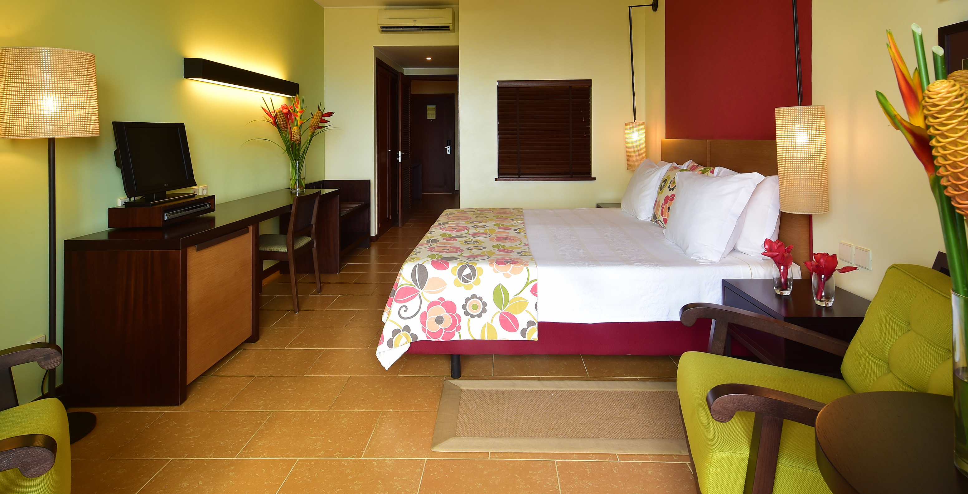 The Sea View Room of Pestana São Tomé has two single beds together, two armchairs, and a desk with a television