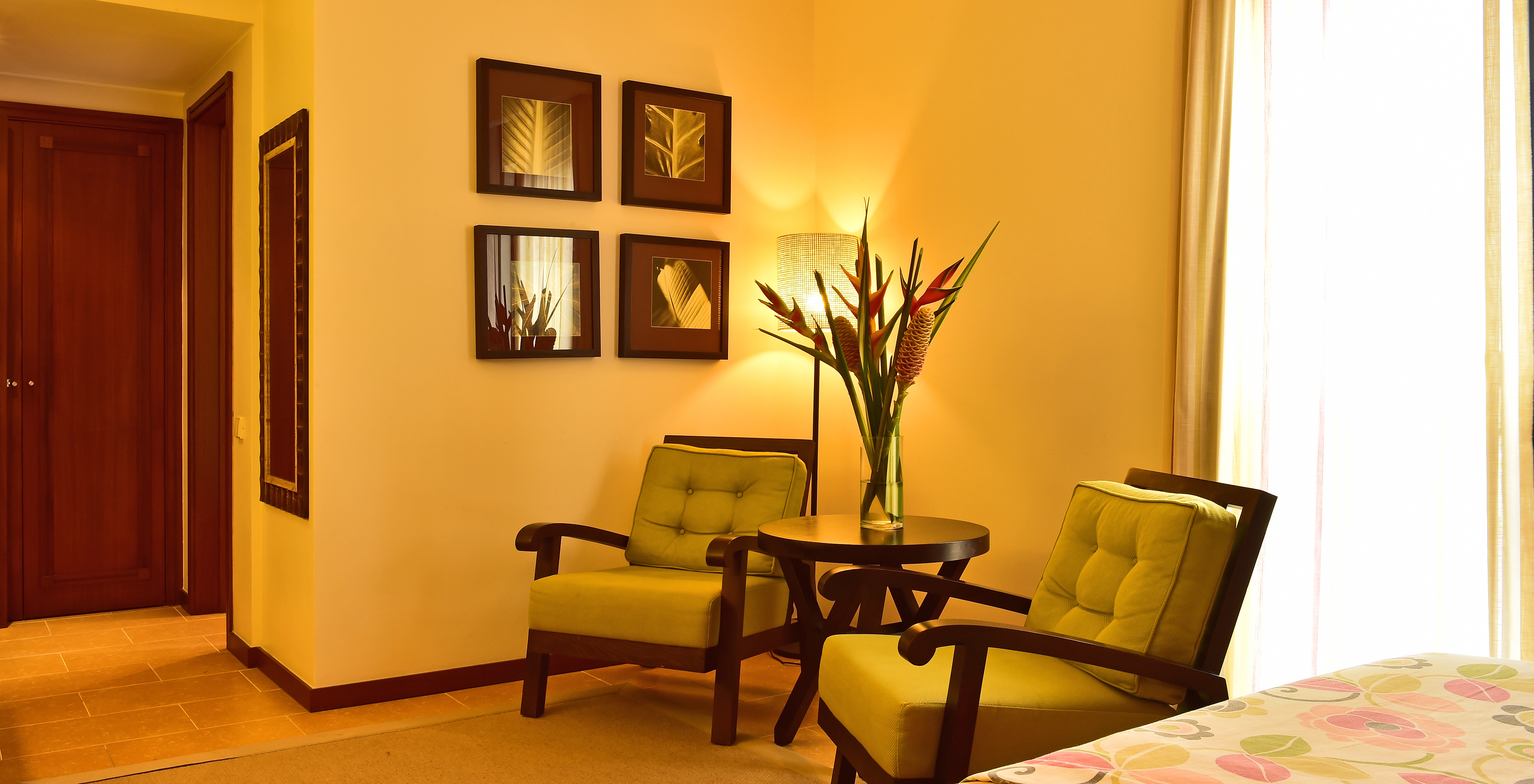 The Junior Suite of Pestana São Tomé has two armchairs at the foot of the bed with a small table and a vase of flowers