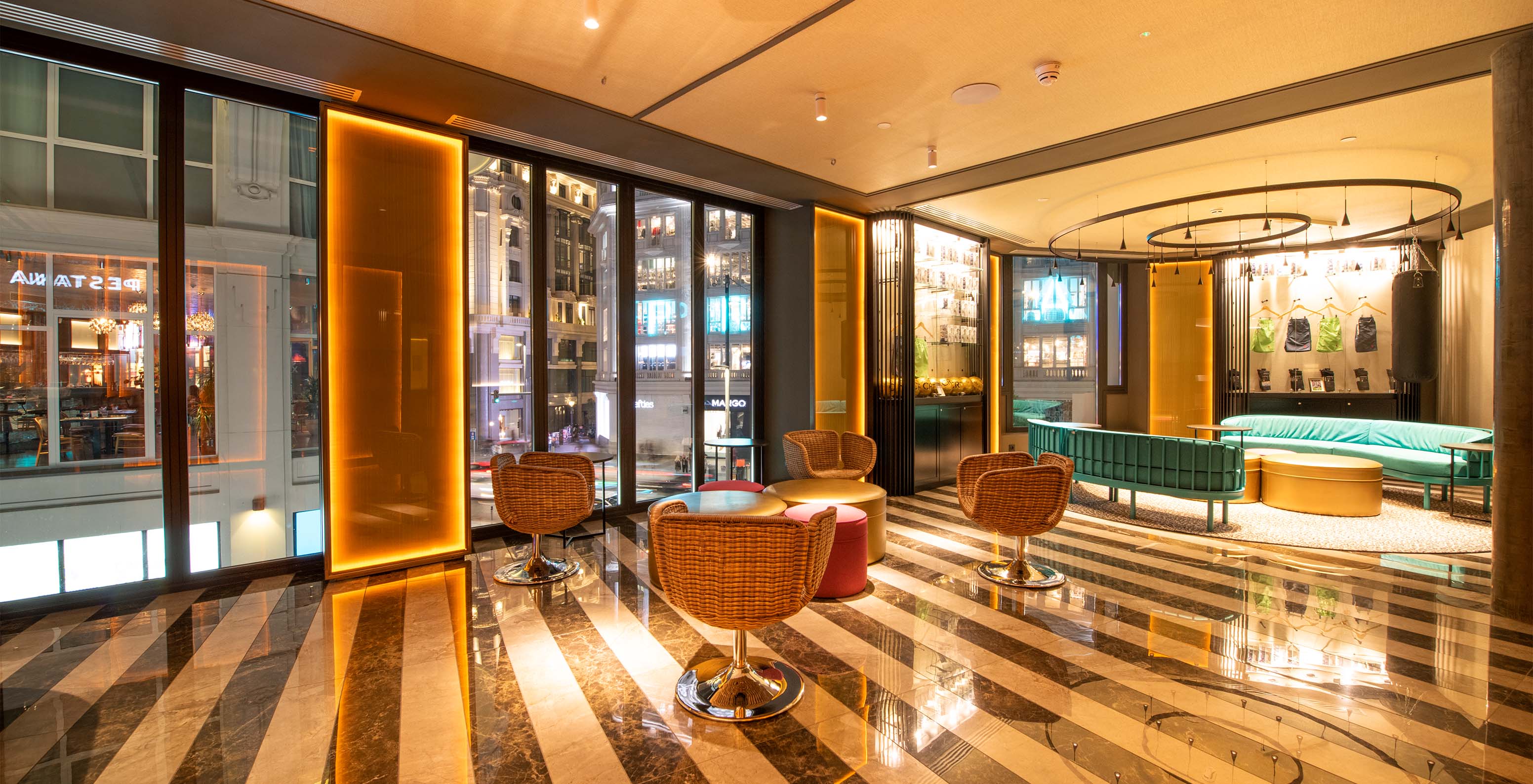 Hotel reception with yellow, blue, and orange chairs and sofas, with side tables and large street-view windows