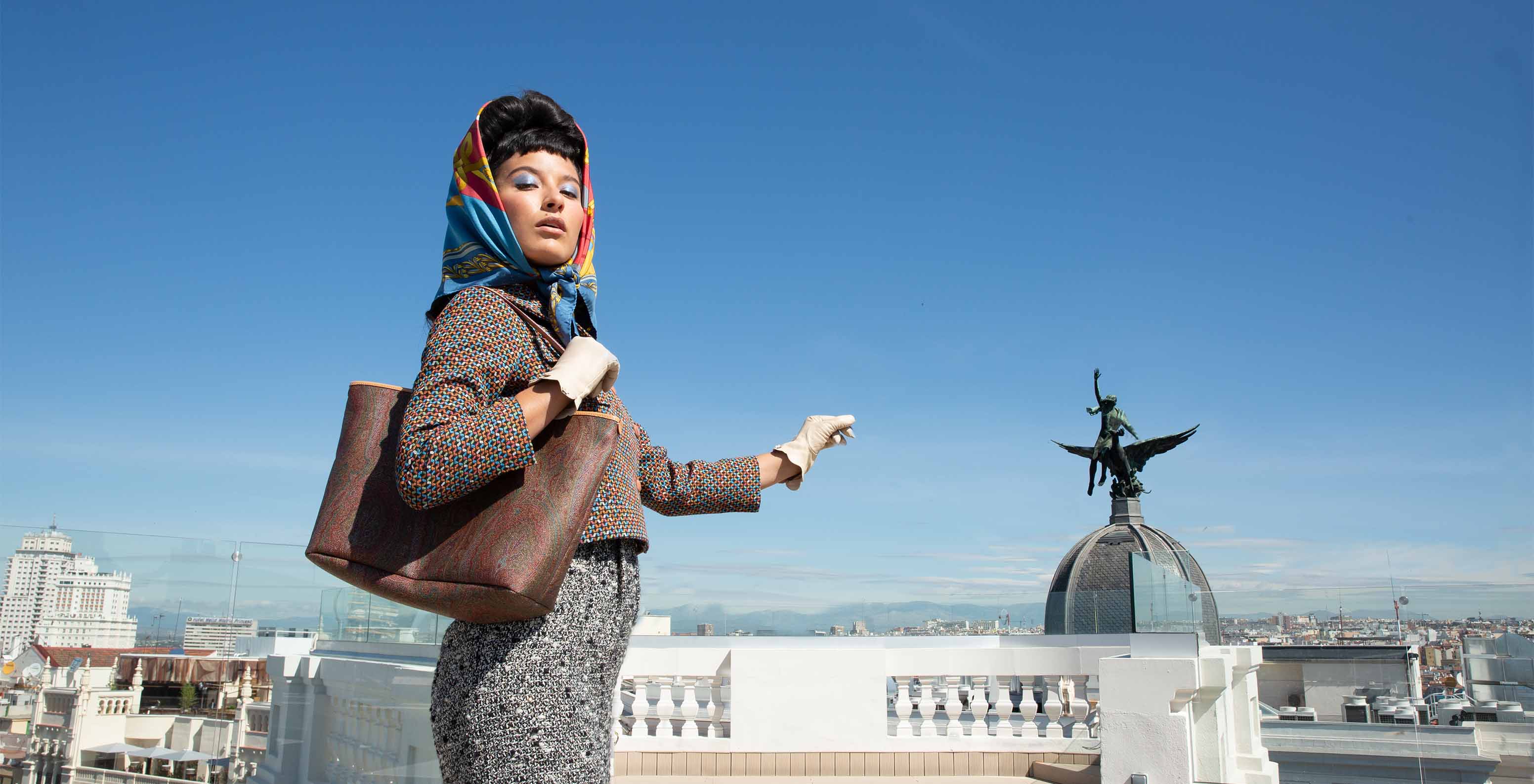 Woman in formal wear with headscarf on hotel rooftop, facing a statue on a building dome