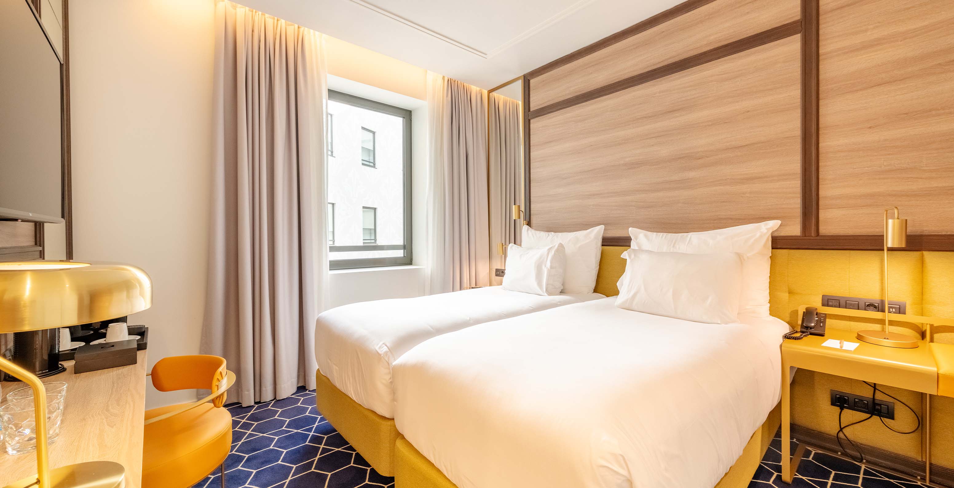 The Superior Room at Pestana CR7 Gran Vía Madrid features two beds, a chair, and a window facing the interior courtyard