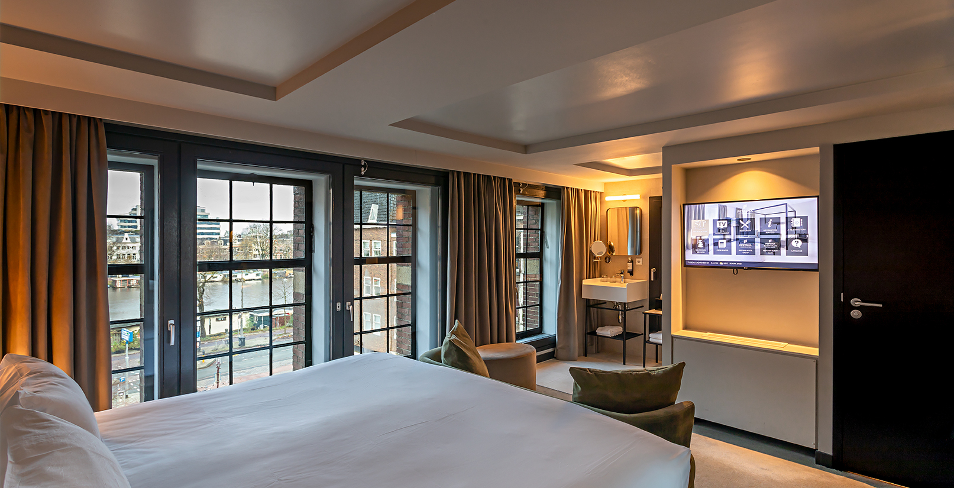 Deluxe room at Pestana Amsterdam Riverside has a TV in front of the bed and large windows overlooking the street