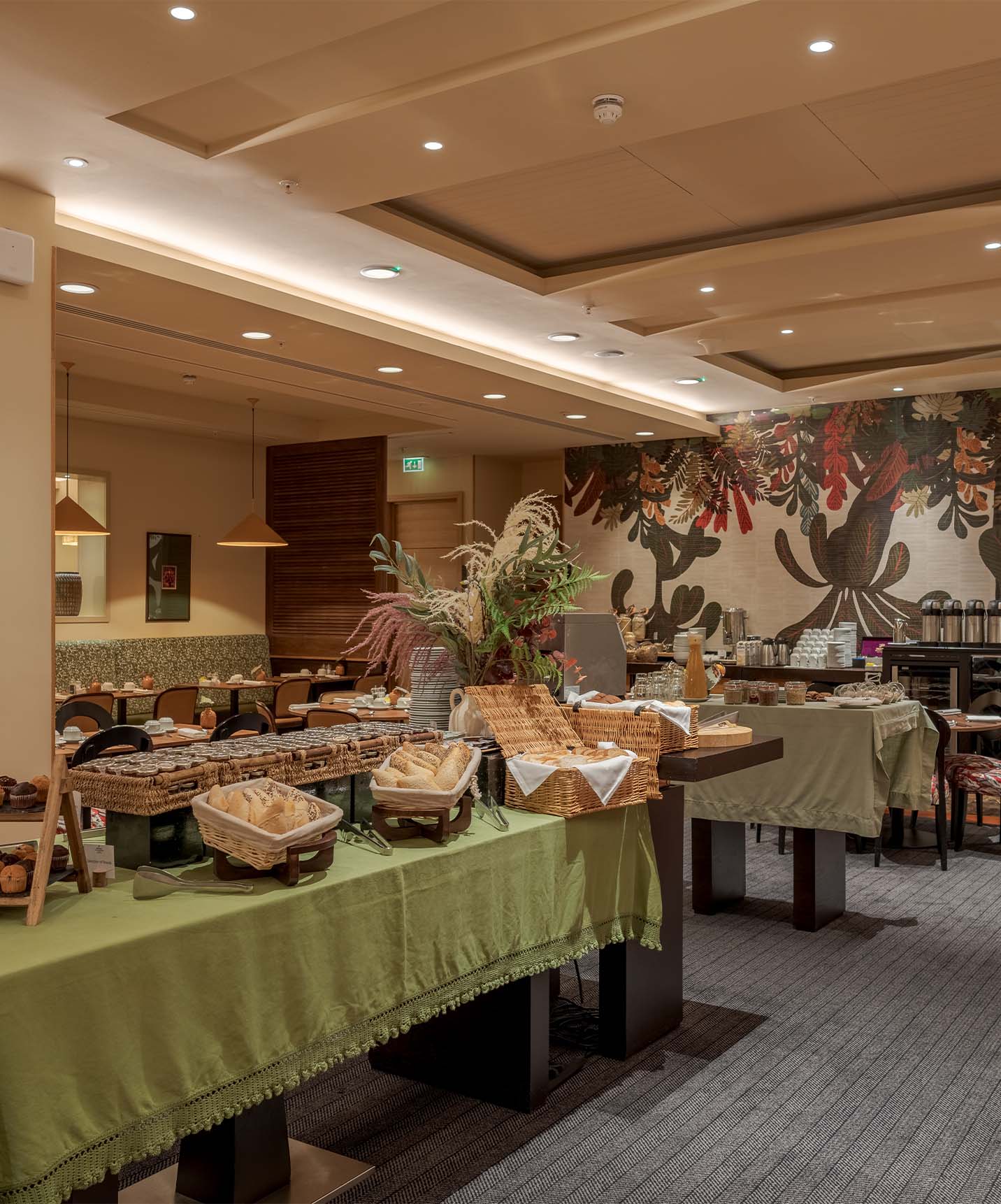 Hotel restaurant with several tables of food like bread, cakes, juices, and other drinks with floral wallpaper