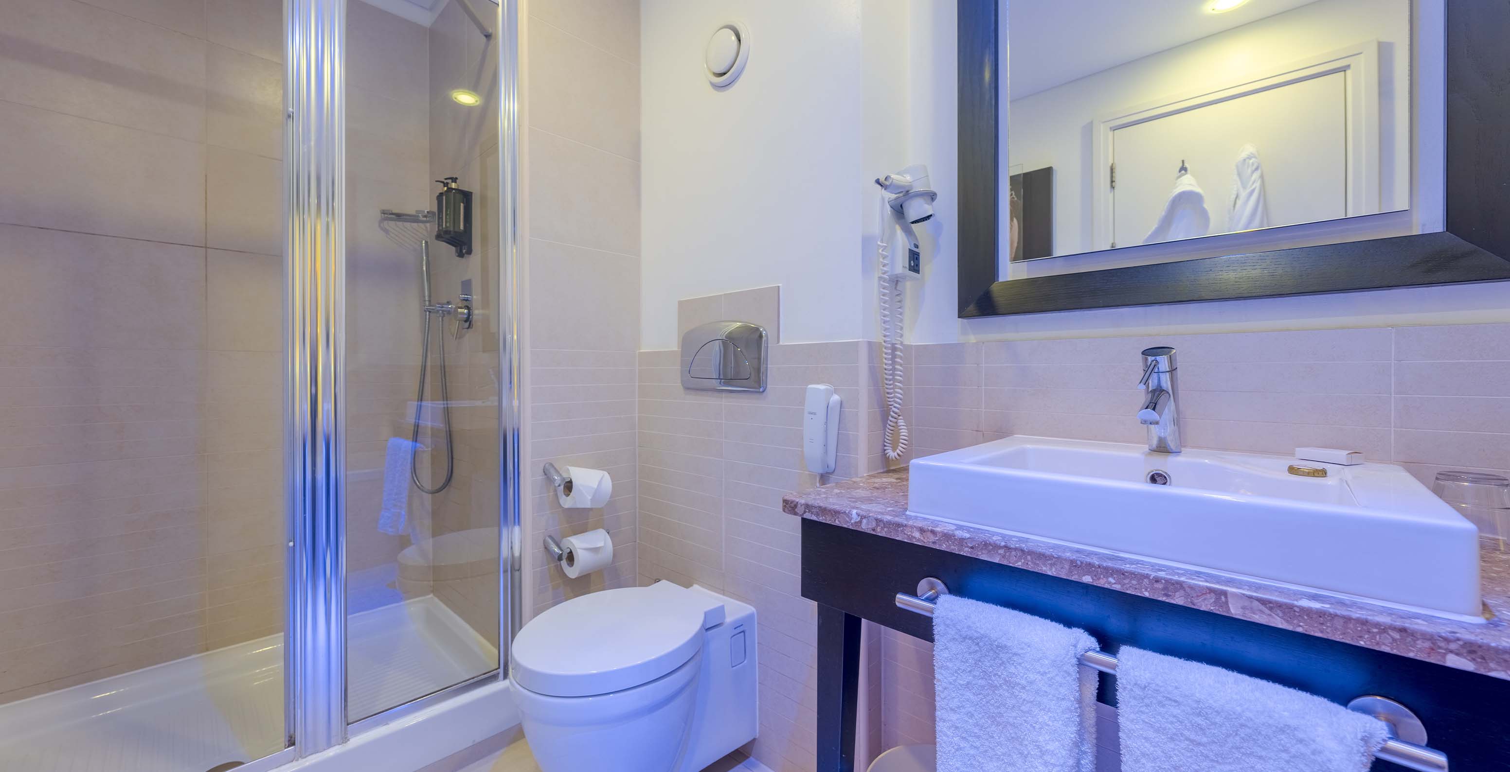 The Deluxe Family at Pestana Chelsea Bridge has a bathroom with a shower with glass doors, toilet, sink, and mirror