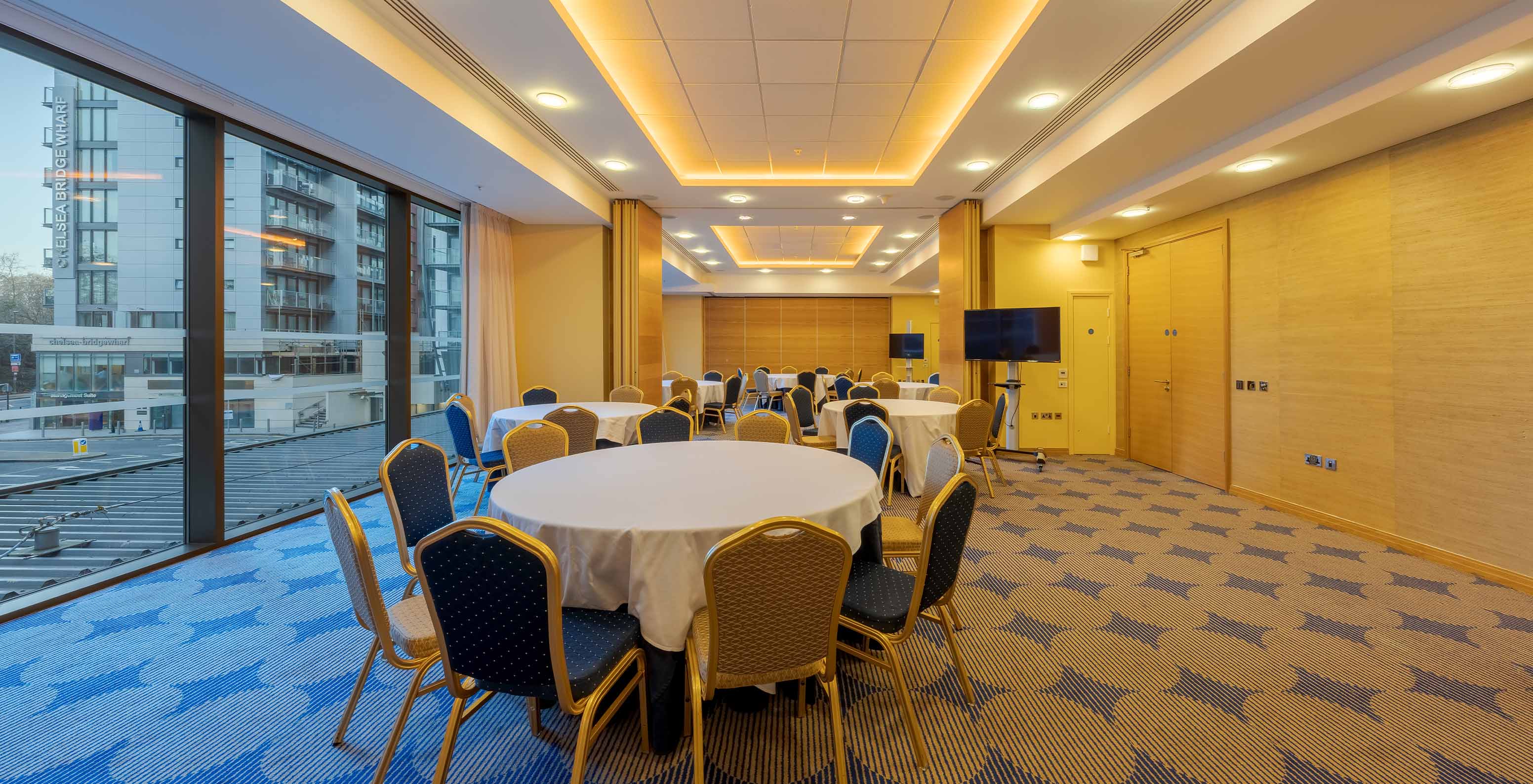 Meeting room with round tables, wooden dividers, TVs, and large windows with a city view