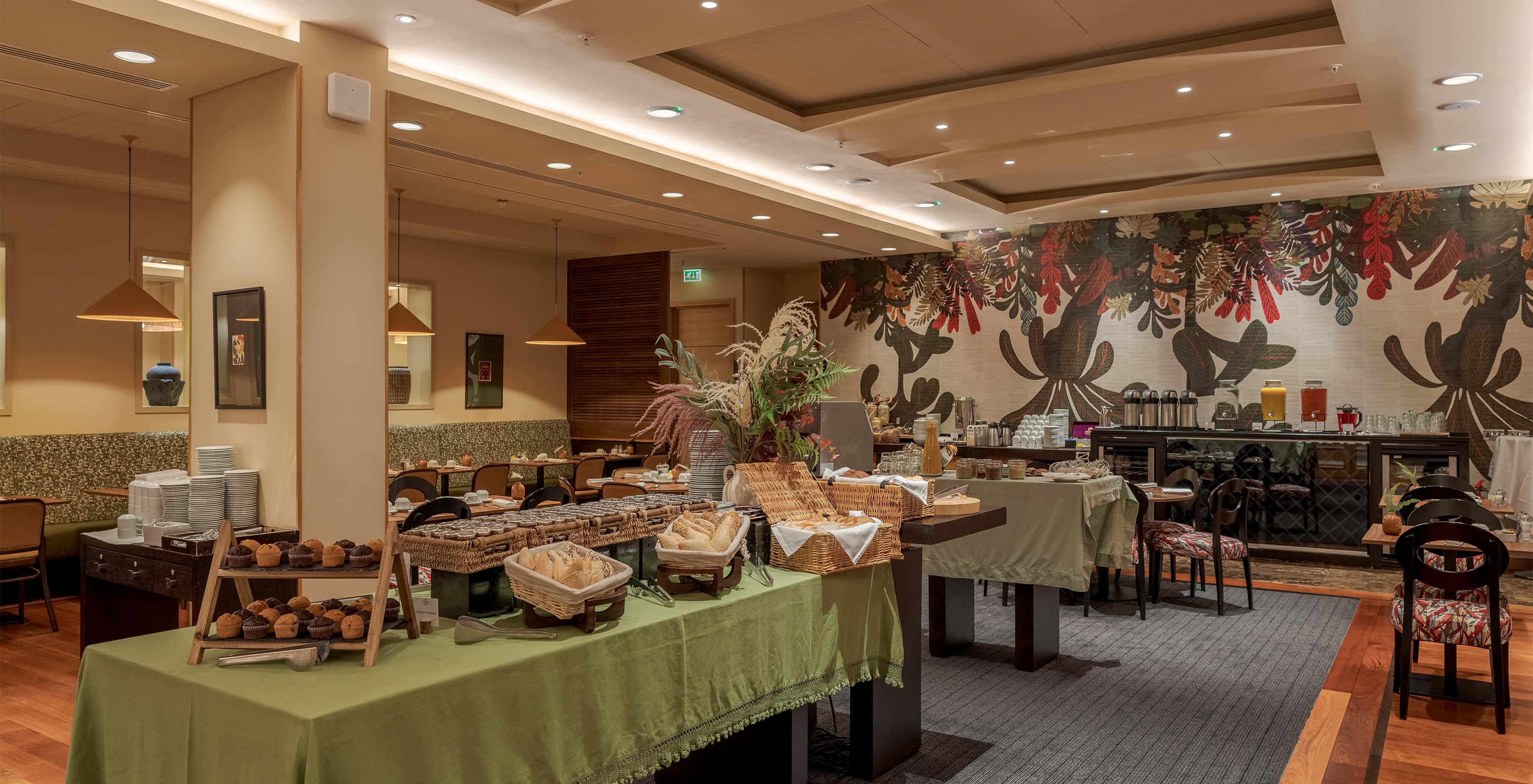 Hotel restaurant with various tables of food, like bread, cakes, juices, and other drinks, with floral wallpaper