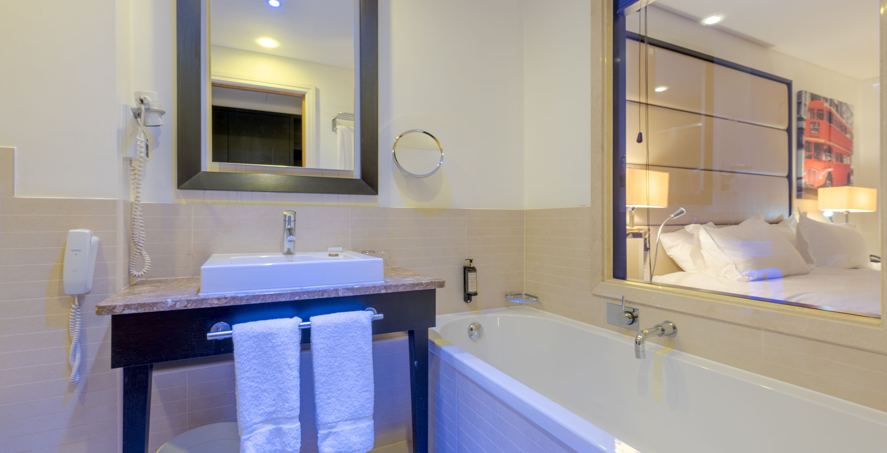 The Deluxe Superior King at Pestana Chelsea Bridge has a bathroom with a bathtub, glass to the room, sink, and mirrors