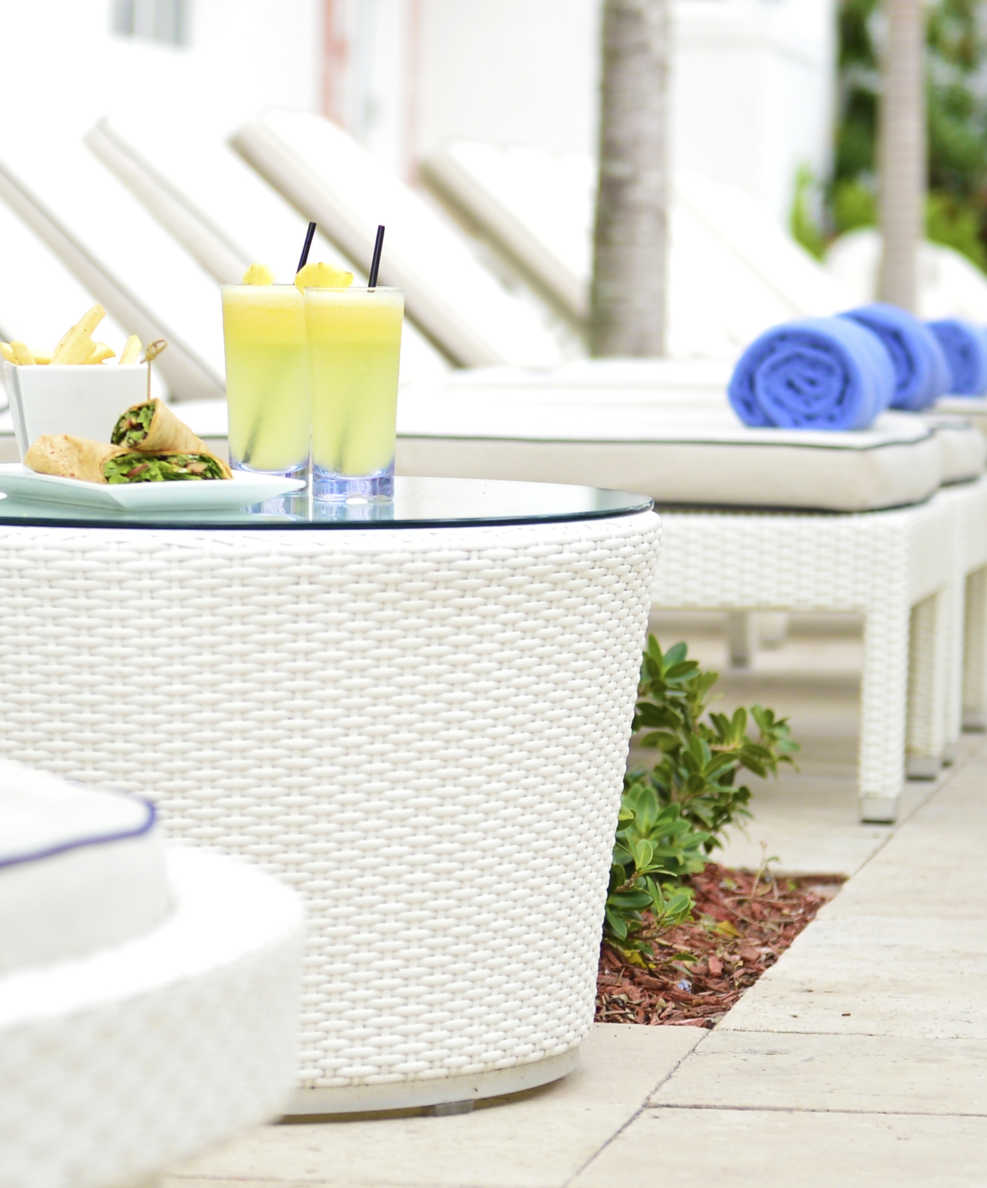 Outdoor bar area with white sun loungers, coffee tables, and two cocktails, wraps, and French fries