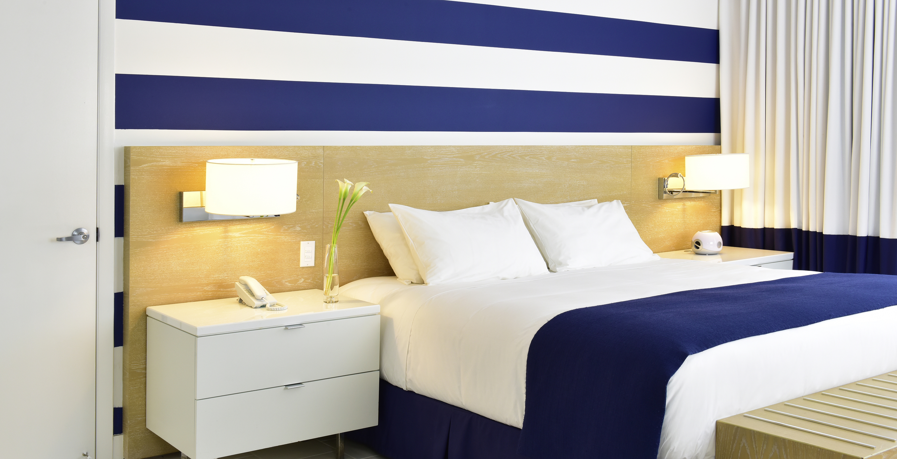 The Pestana Deluxe King Bed Room at Pestana Miami South Beach has a king size bed, lamp and bedside table