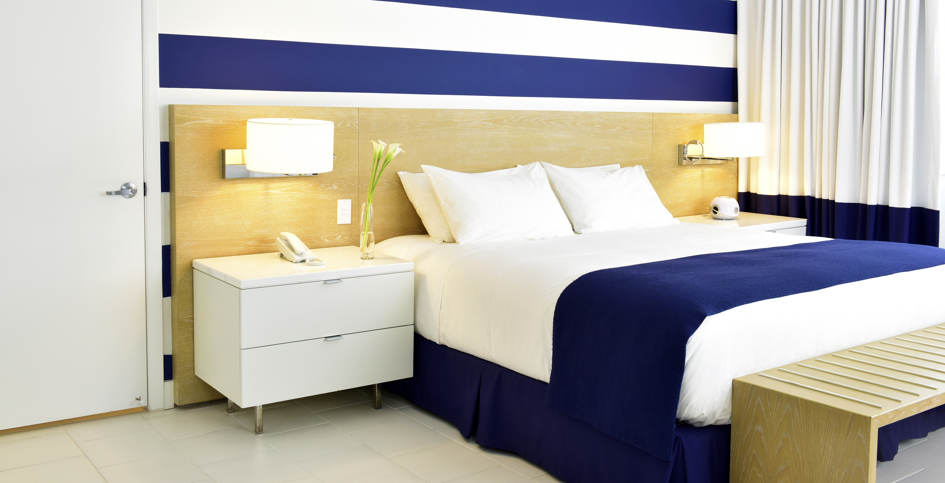 The Pestana Deluxe Queen Bed Room at Pestana Miami South Beach has a double bed, lamp and bedside table