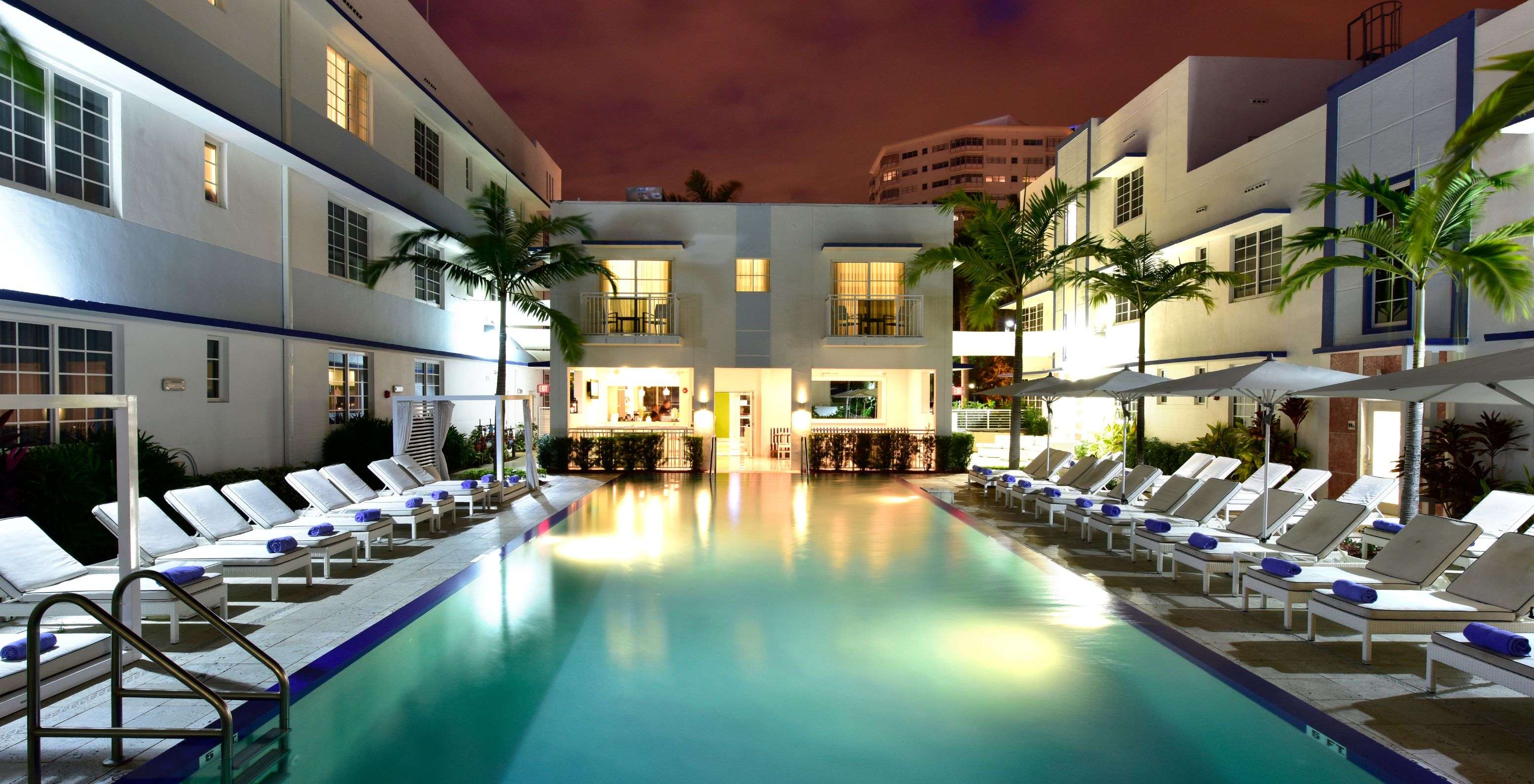 Outdoor area of the hotel featuring a pool, loungers with shade, and palm trees