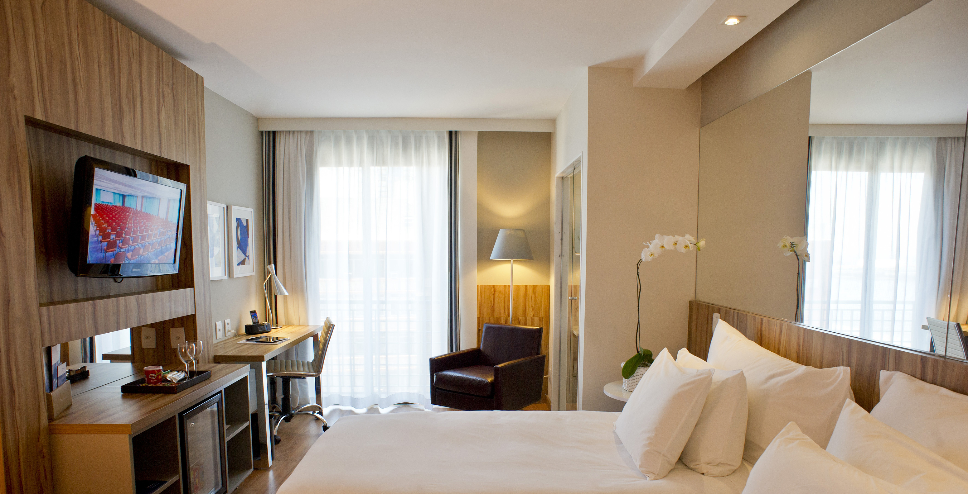 The Standard Twin Room of Pestana Rio Atlântica has two beds, mirror on the headboard, a television in front, and an armchair