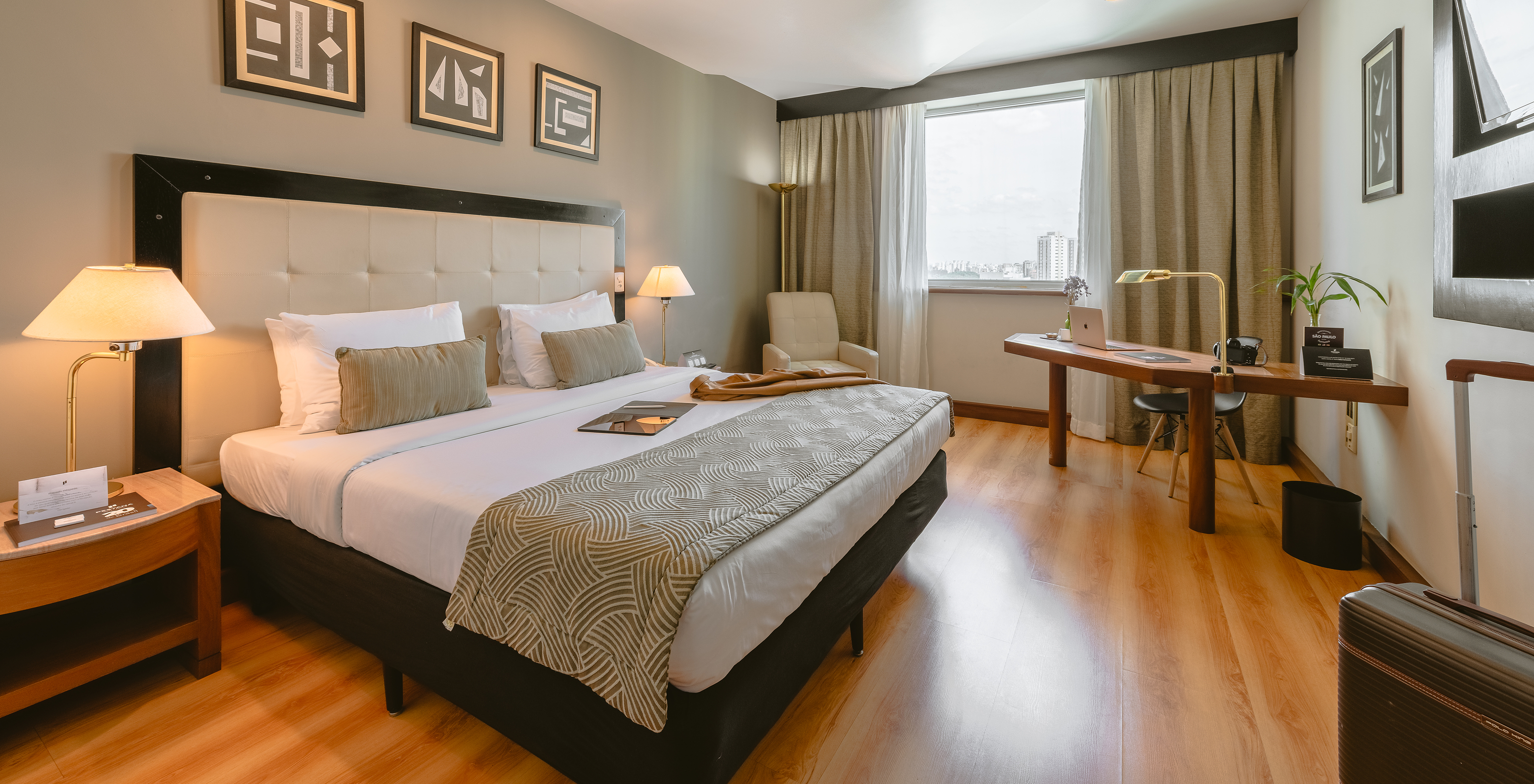 The Standard Room of Pestana São Paulo has a double bed, two bedside tables, an armchair, and a desk