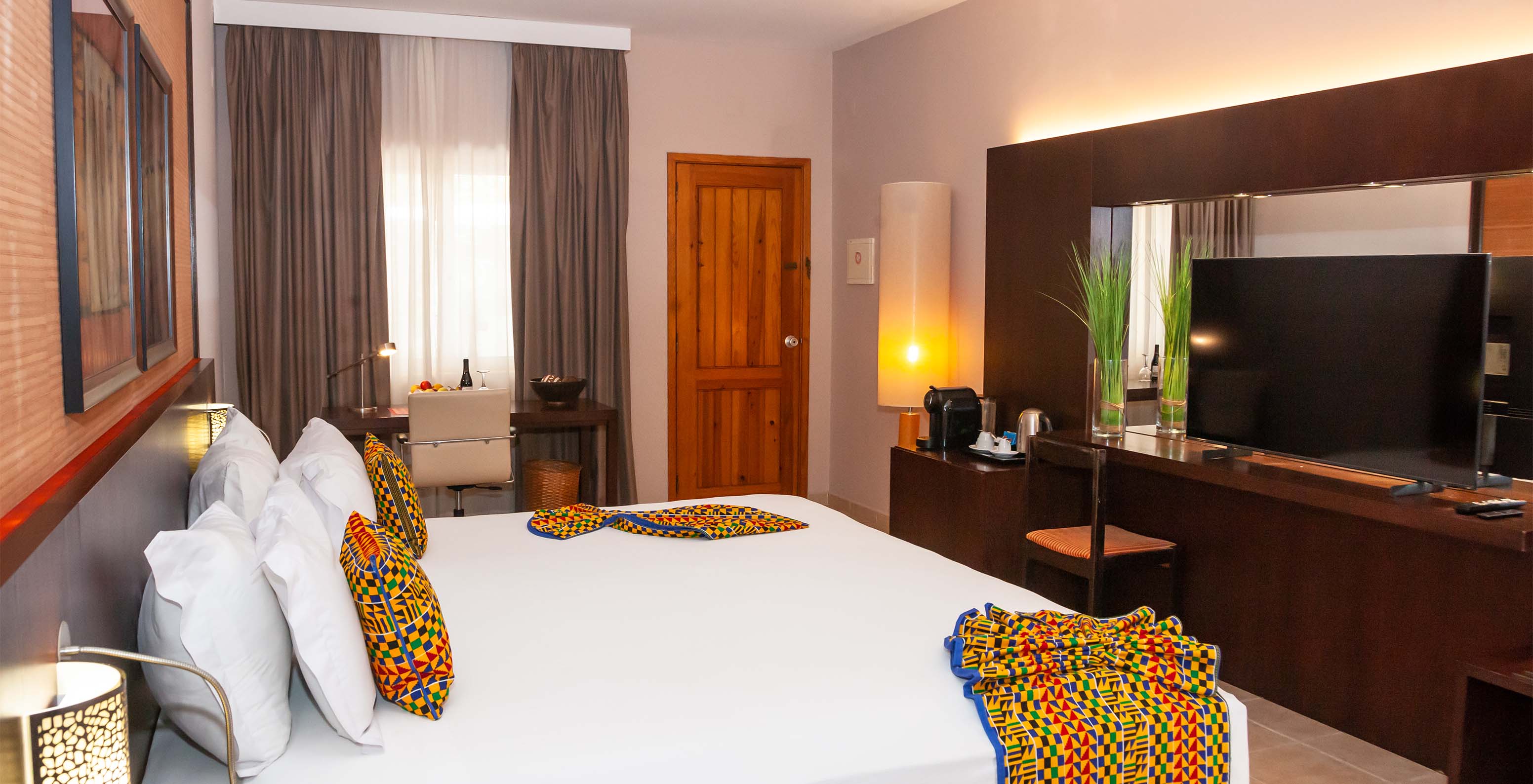 The Junior Suite at Pestana Tropico features a double bed, television, mirror, desk with chair, and fruit basket