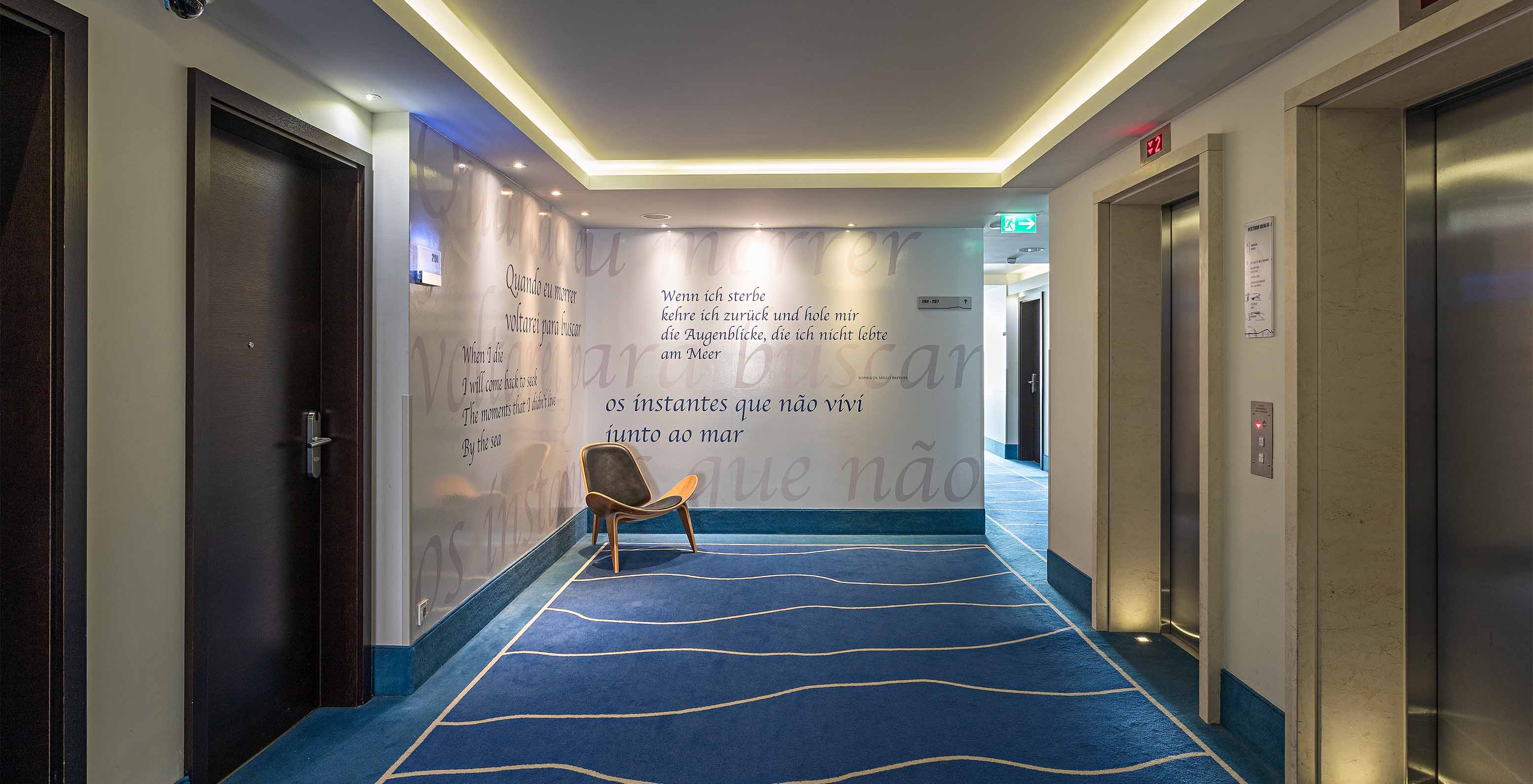 Hallway at Pestana Berlin, with an armchair, two elevators, and walls with German phrases