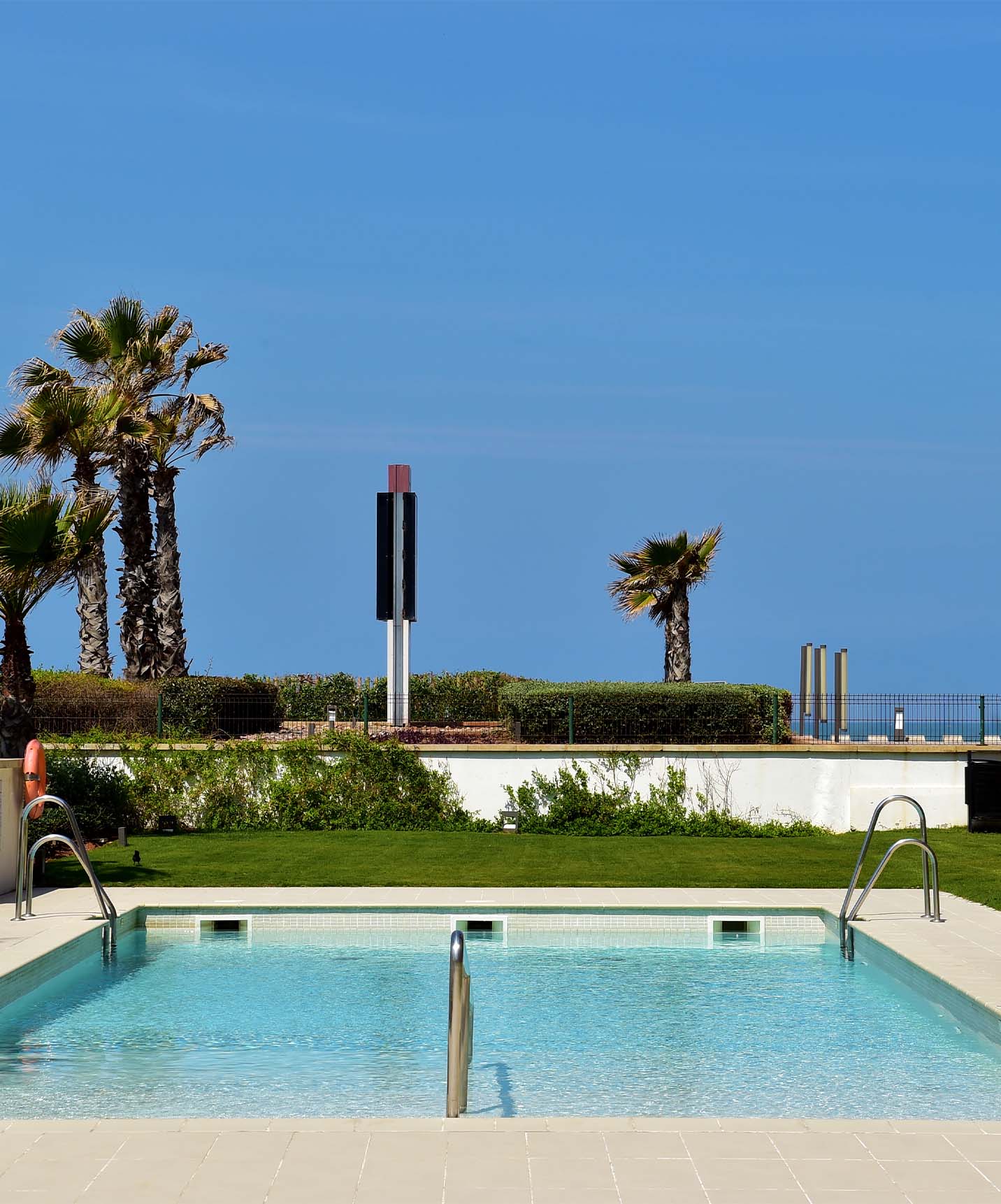 Pool of Pestana Casablanca hotel in Morocco with the sea in the background, blue sky, and palm trees