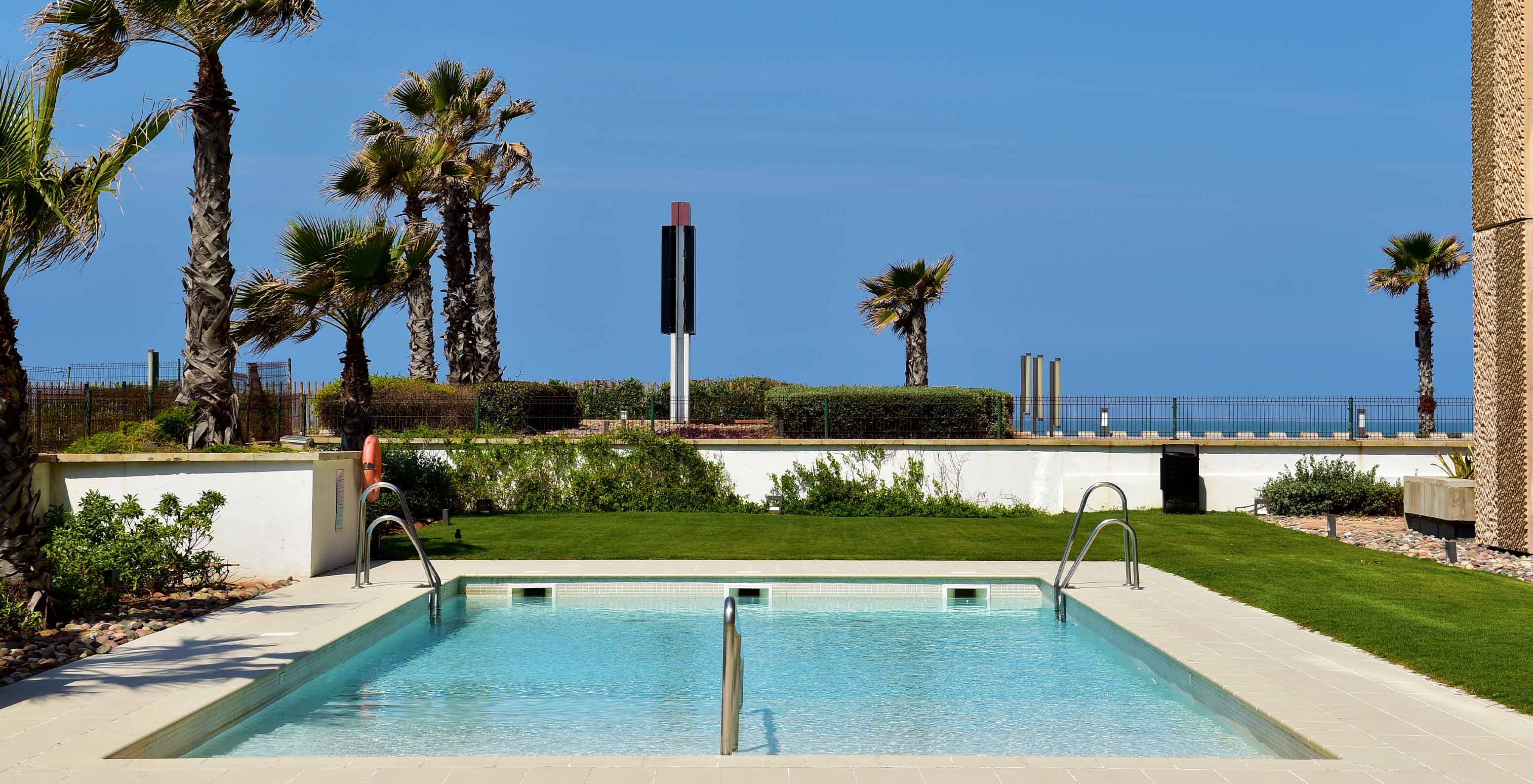 Pool at Pestana Casablanca in Morocco with the sea in the background, blue sky, and palm trees