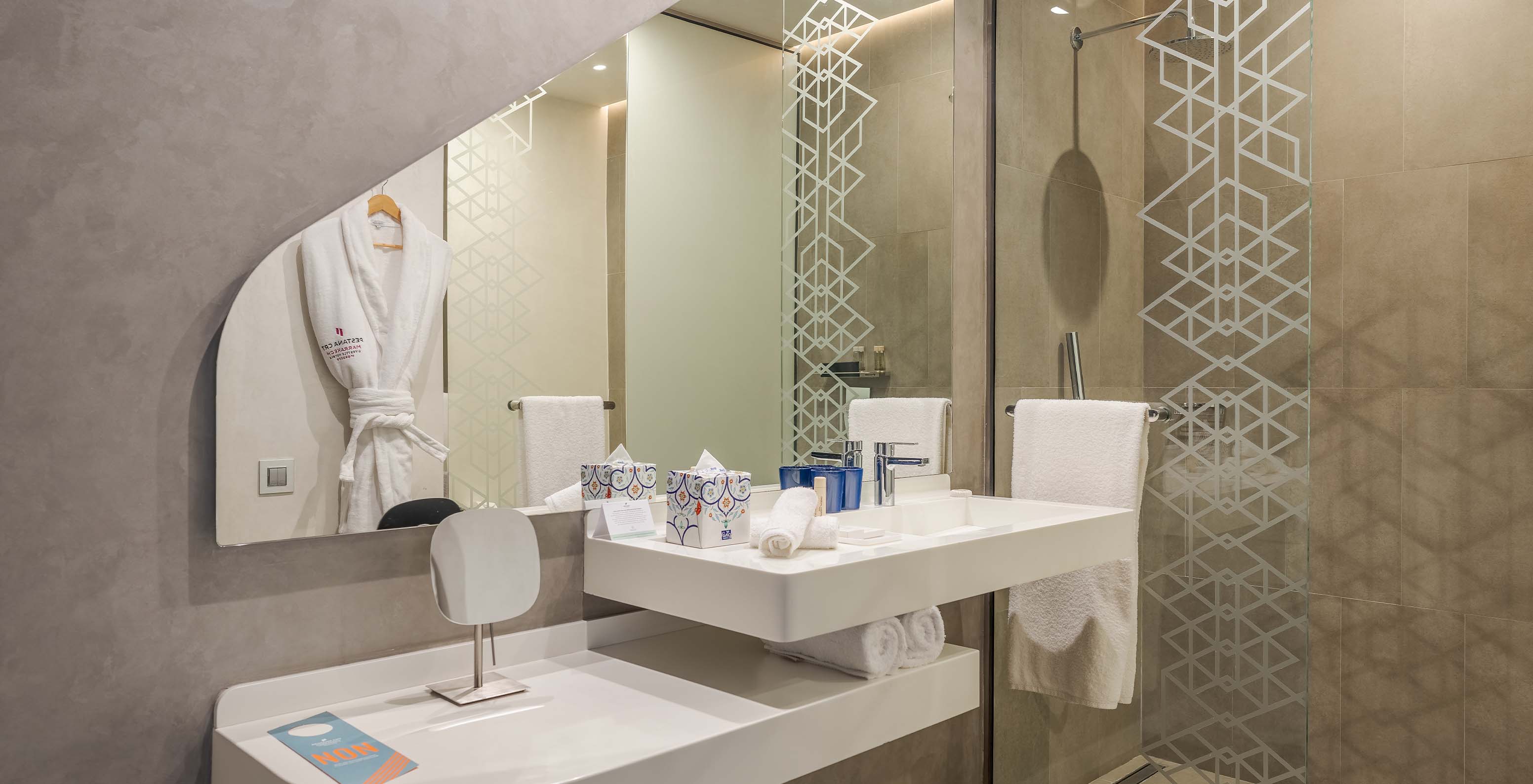 The CR7 Junior Suite at Pestana CR7 Marrakech has a bathroom with a walk-in shower, sink with mirror, and shelf